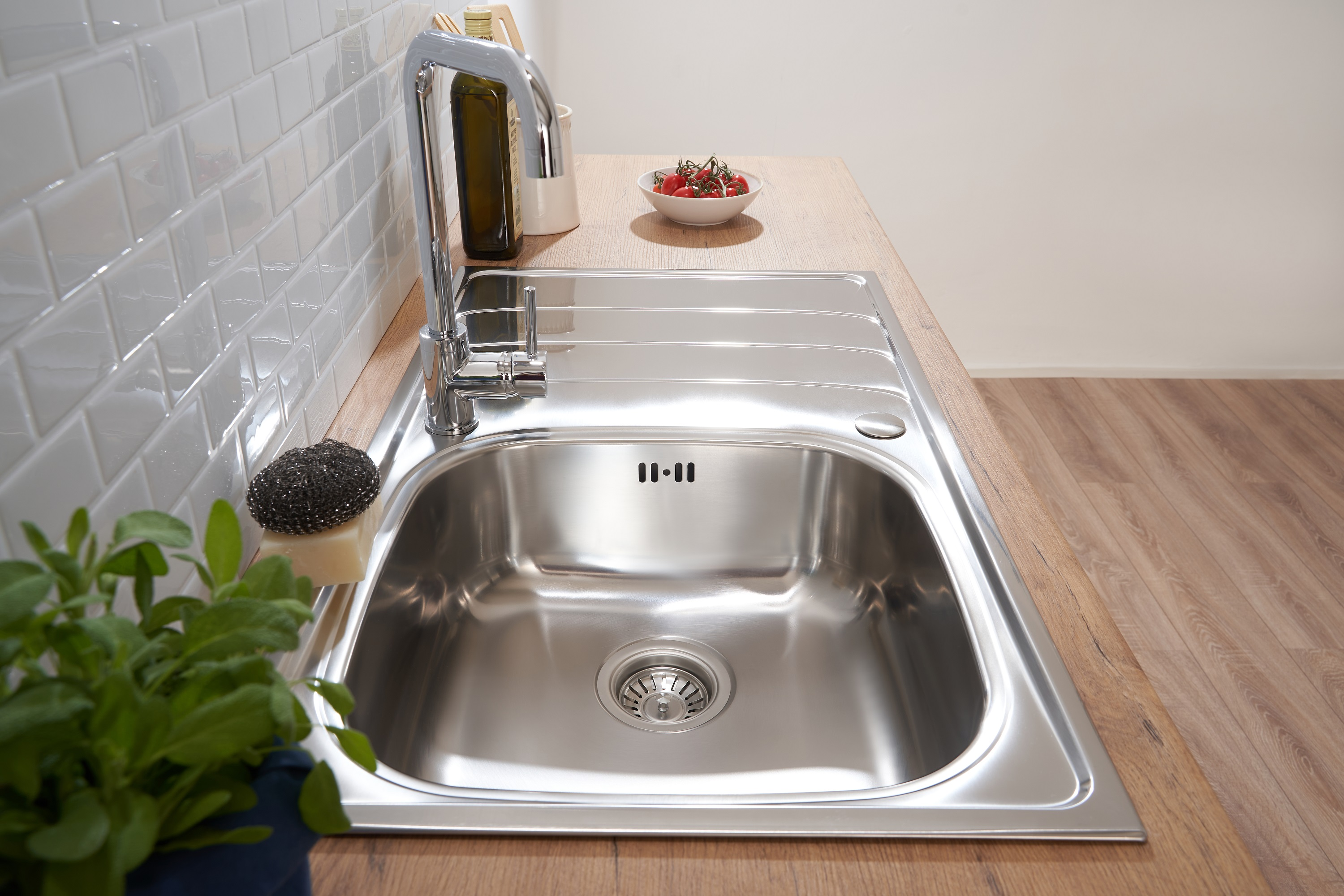 Ein Edelstahlbecken mit Wasserhahn und eine Schüssel Tomaten auf einer Holztheke.