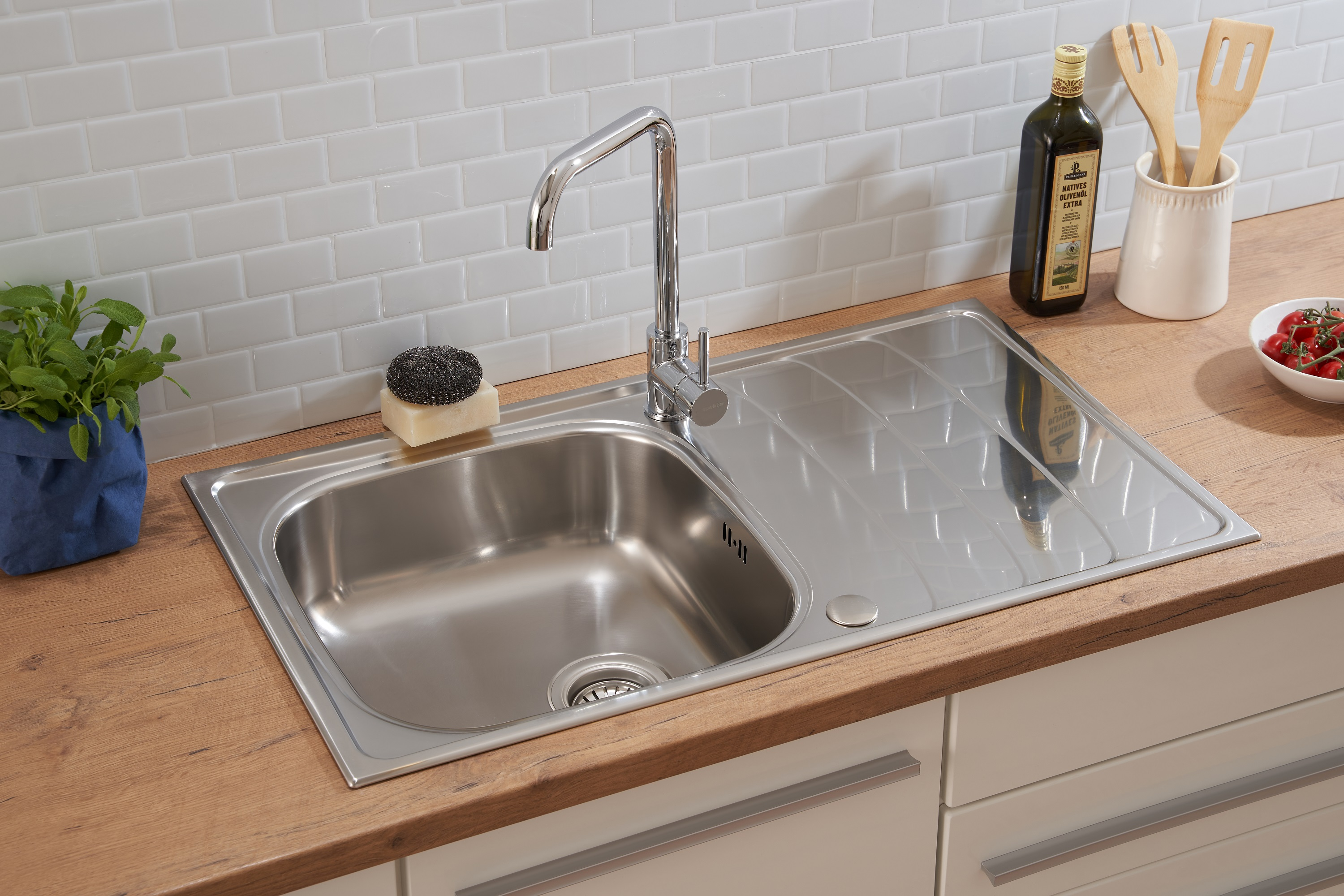 Edelstahl-Küchenspüle mit Wasserhahn, Schwamm und Holz-Arbeitsplatte mit weißen Fliesen.