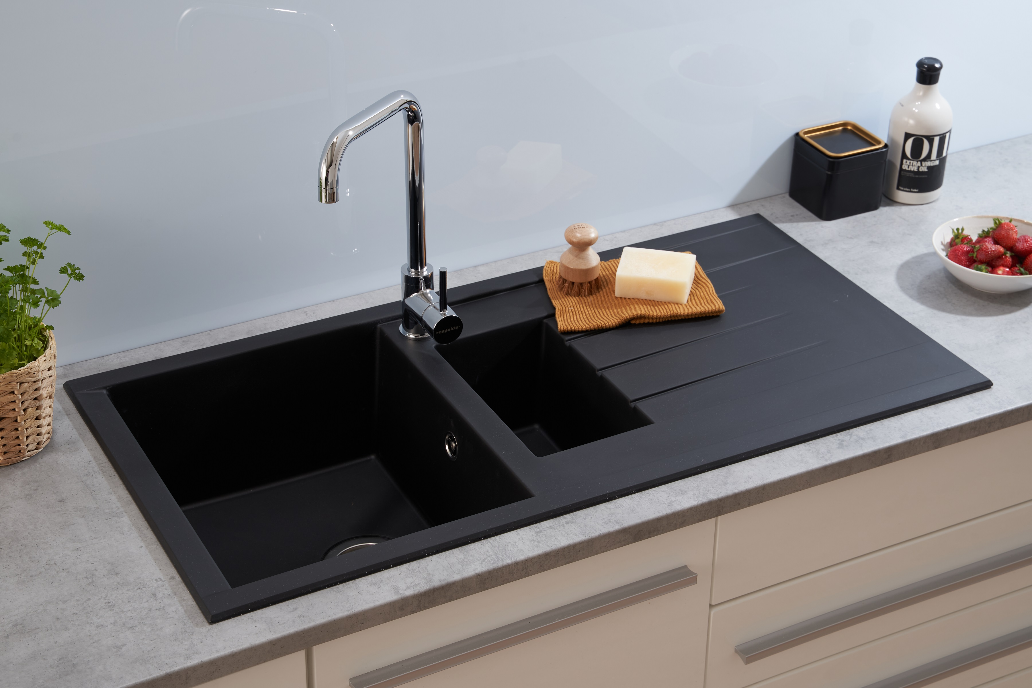 Schwarzes Küchenbecken mit Wasserhahn, Seife und Erdbeeren auf heller Arbeitsplatte.