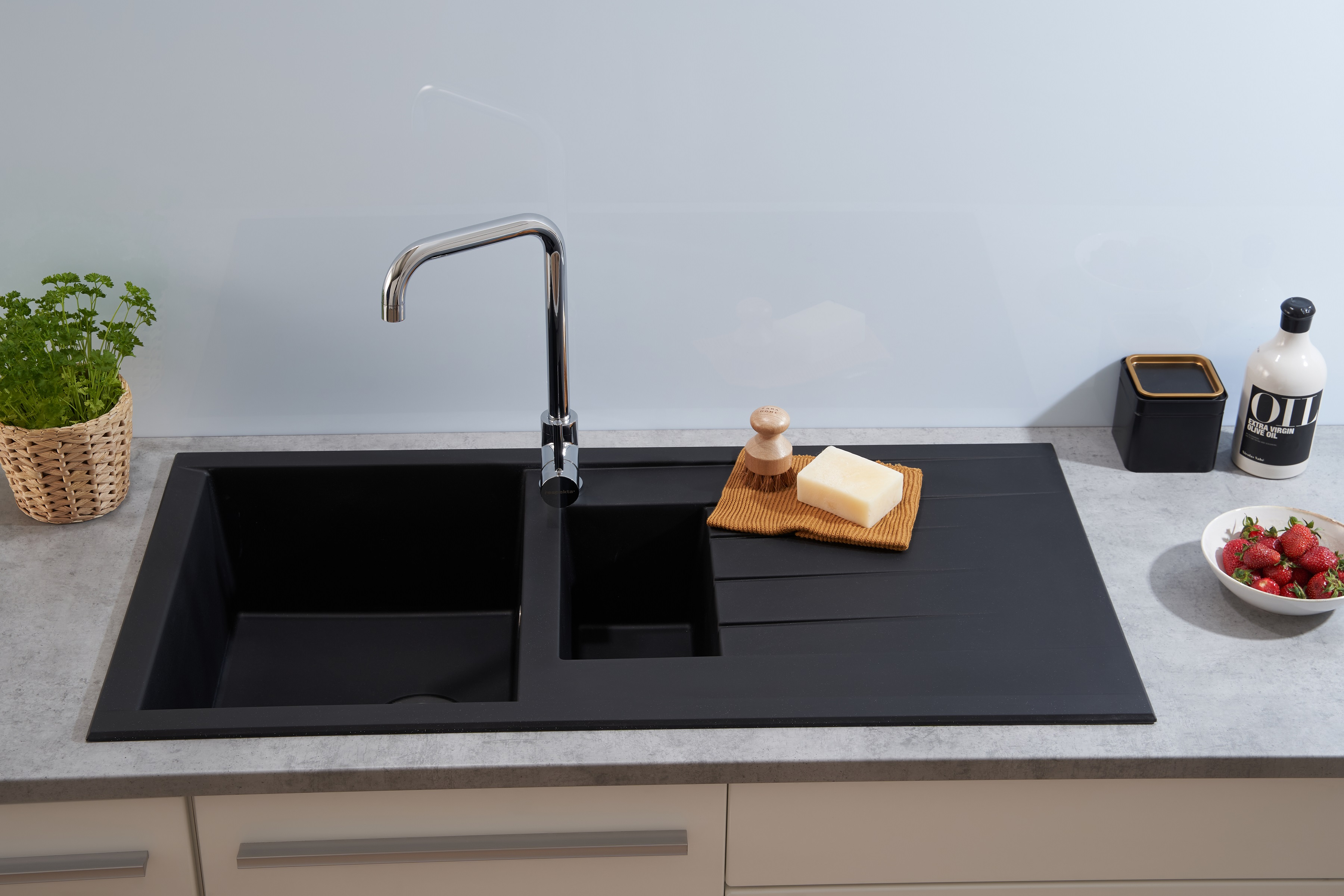 Schwarzes Küchenbecken mit Wasserhahn, Seife und einer Schale Erdbeeren, heller Hintergrund.