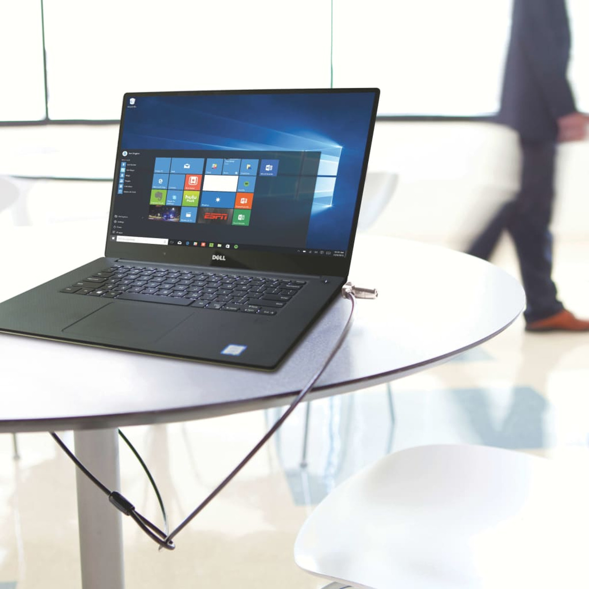 Laptop mit Kabel auf Tisch gesichert, Person im Hintergrund geht vorbei.