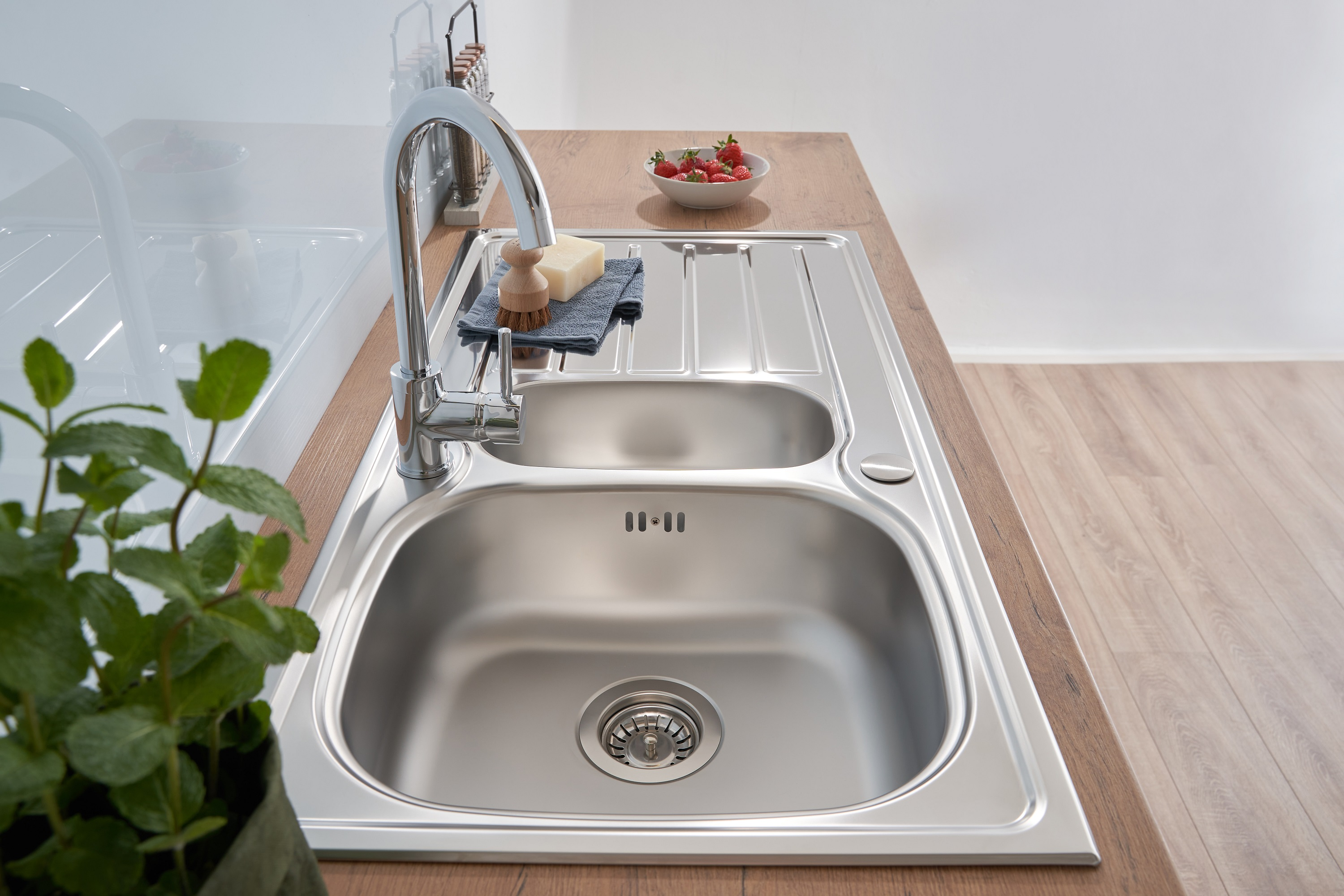 Küchenspüle aus Stahl mit Wasserhahn, Seife, Bürste, Erdbeeren und Pflanze, Holz-Arbeitsplatte.