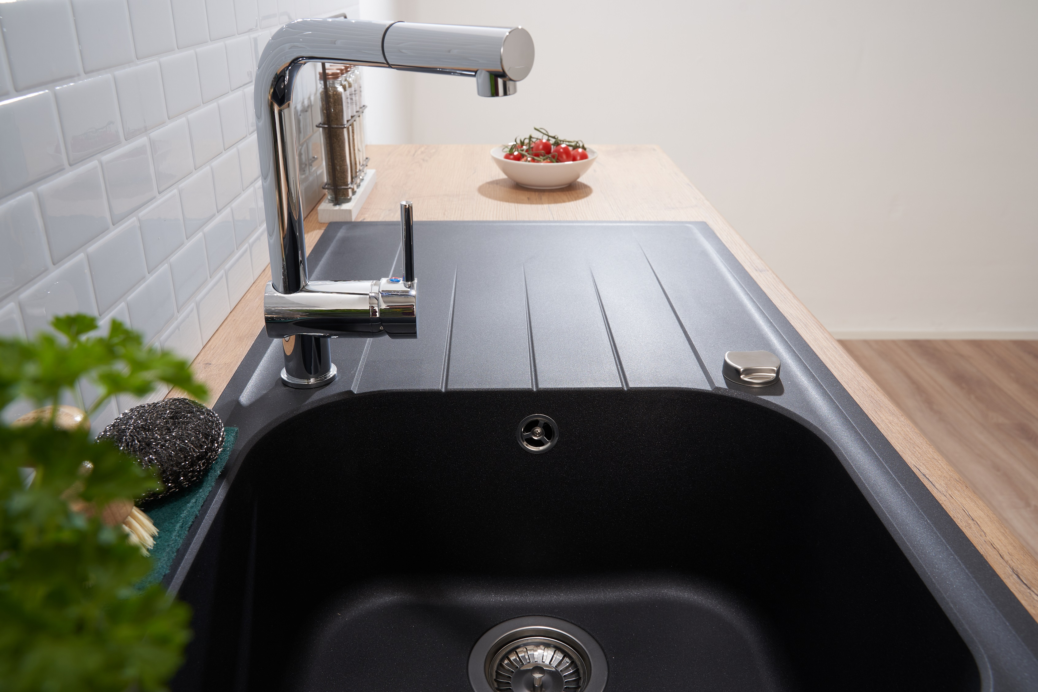 Schwarzes Küchenbecken mit Wasserhahn und Abtropffläche, mit Holzplatte und weißen Fliesen.