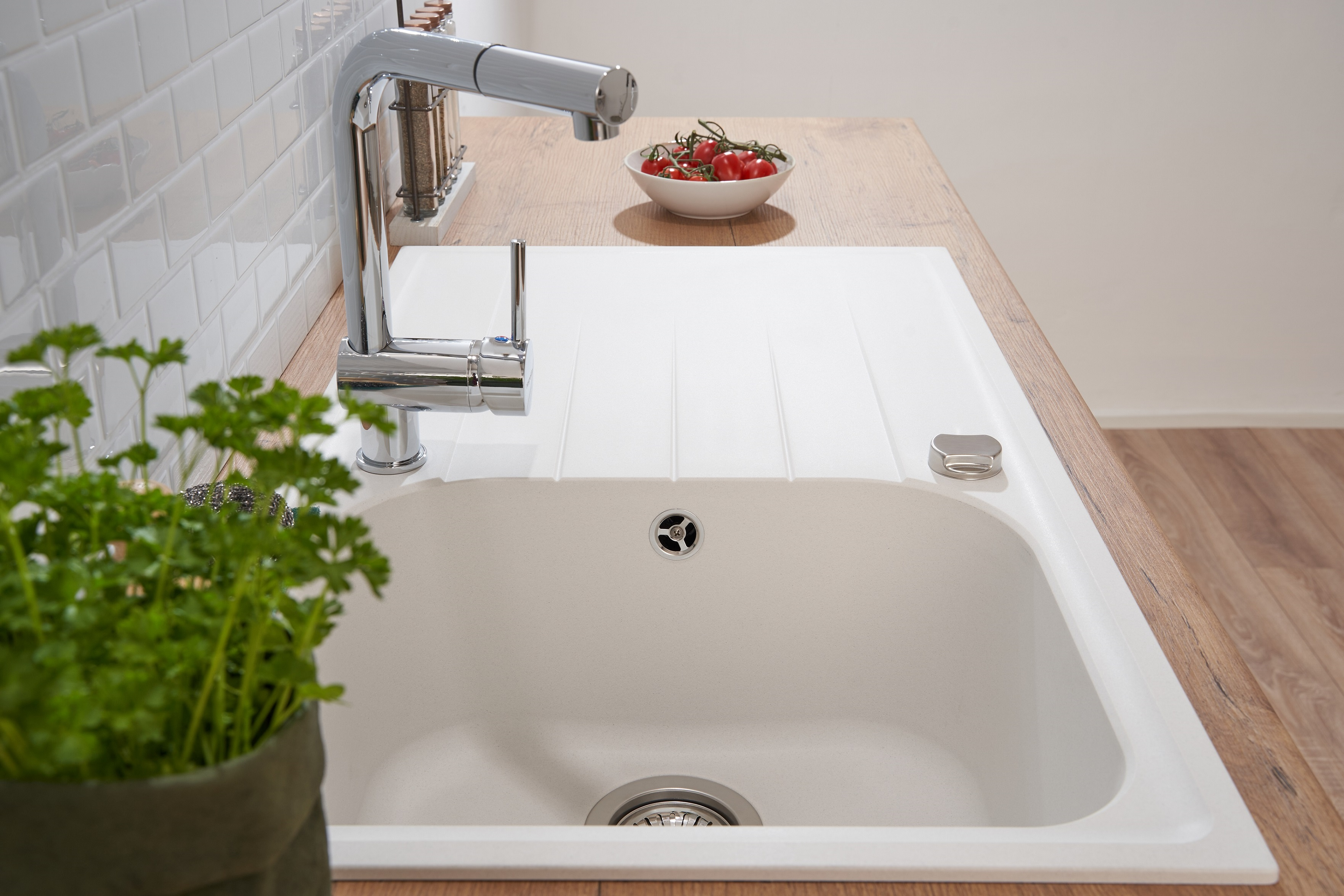 Ein weißes Küchenbecken mit Wasserhahn, Petersilie und Tomaten in einer Schüssel auf einer Holzplatte.