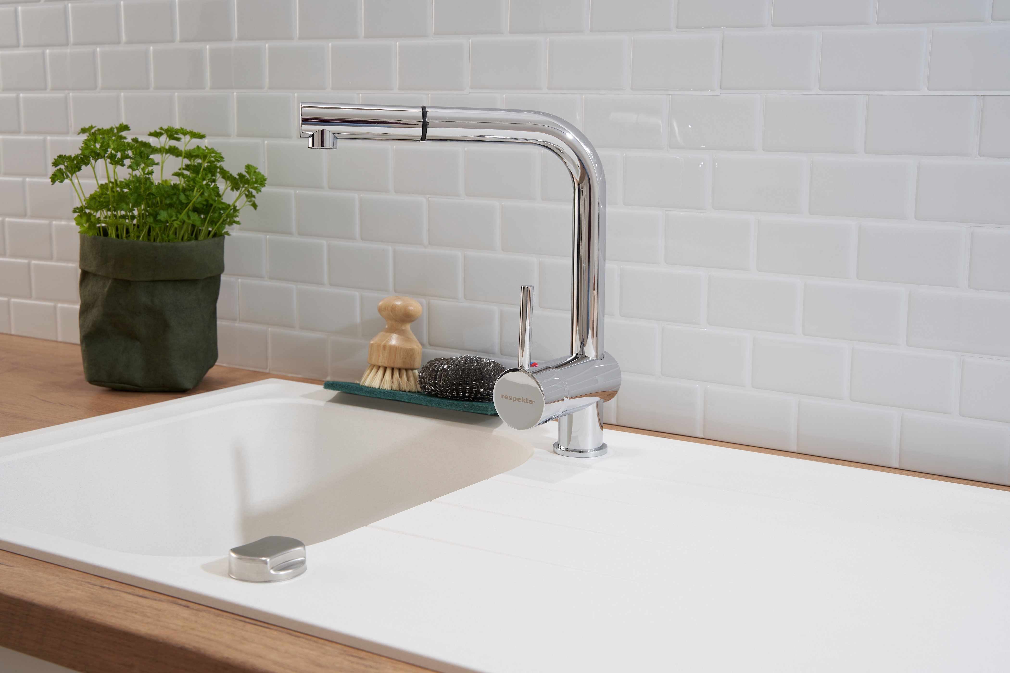 Moderne Küchenspüle mit Wasserhahn, Petersilie im grünen Topf und weißer Fliesenrückwand.