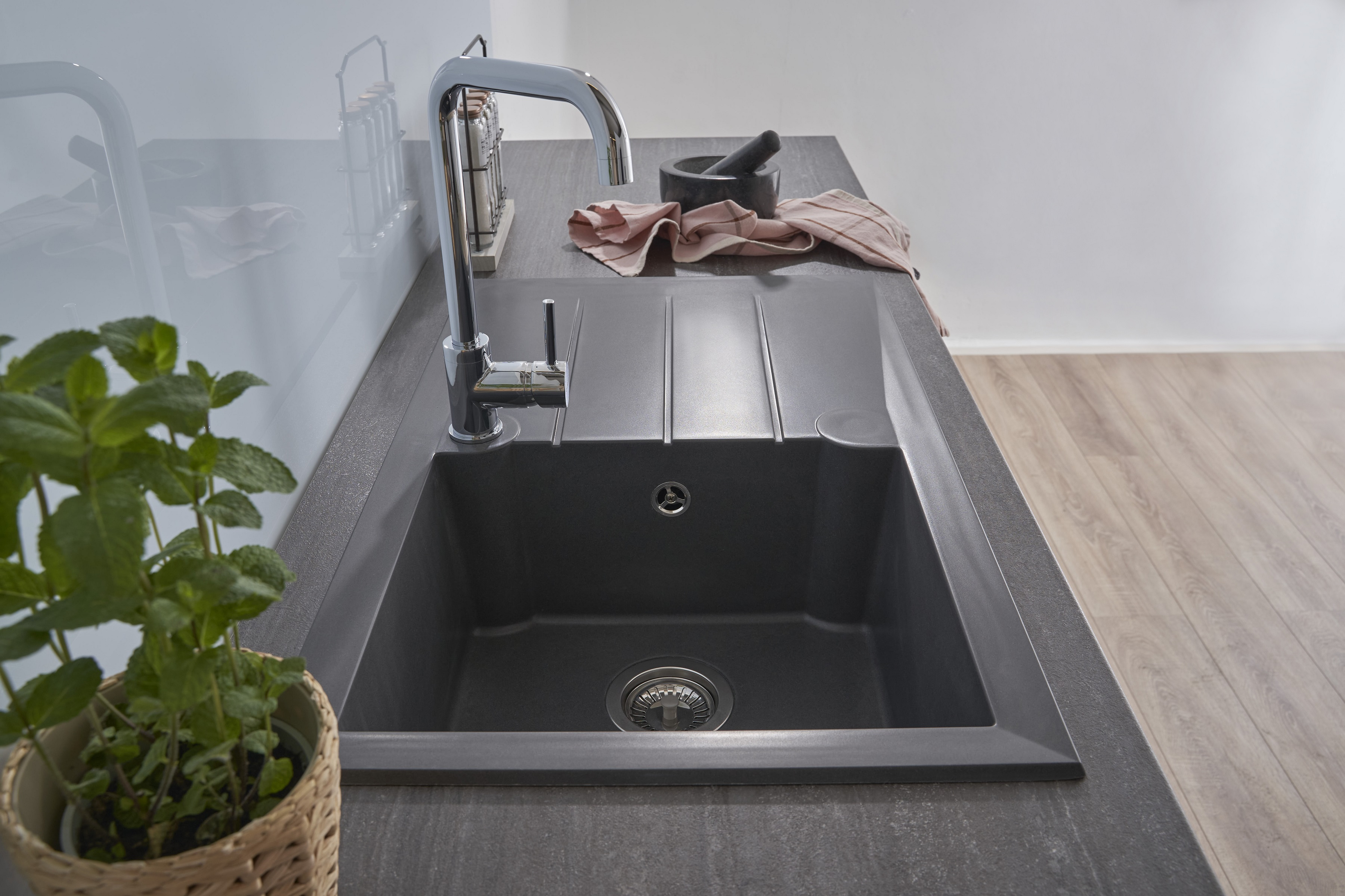 Küchenspüle mit Wasserhahn, schwarzer Schüssel und Arbeitsplatte. Topfpflanze links.