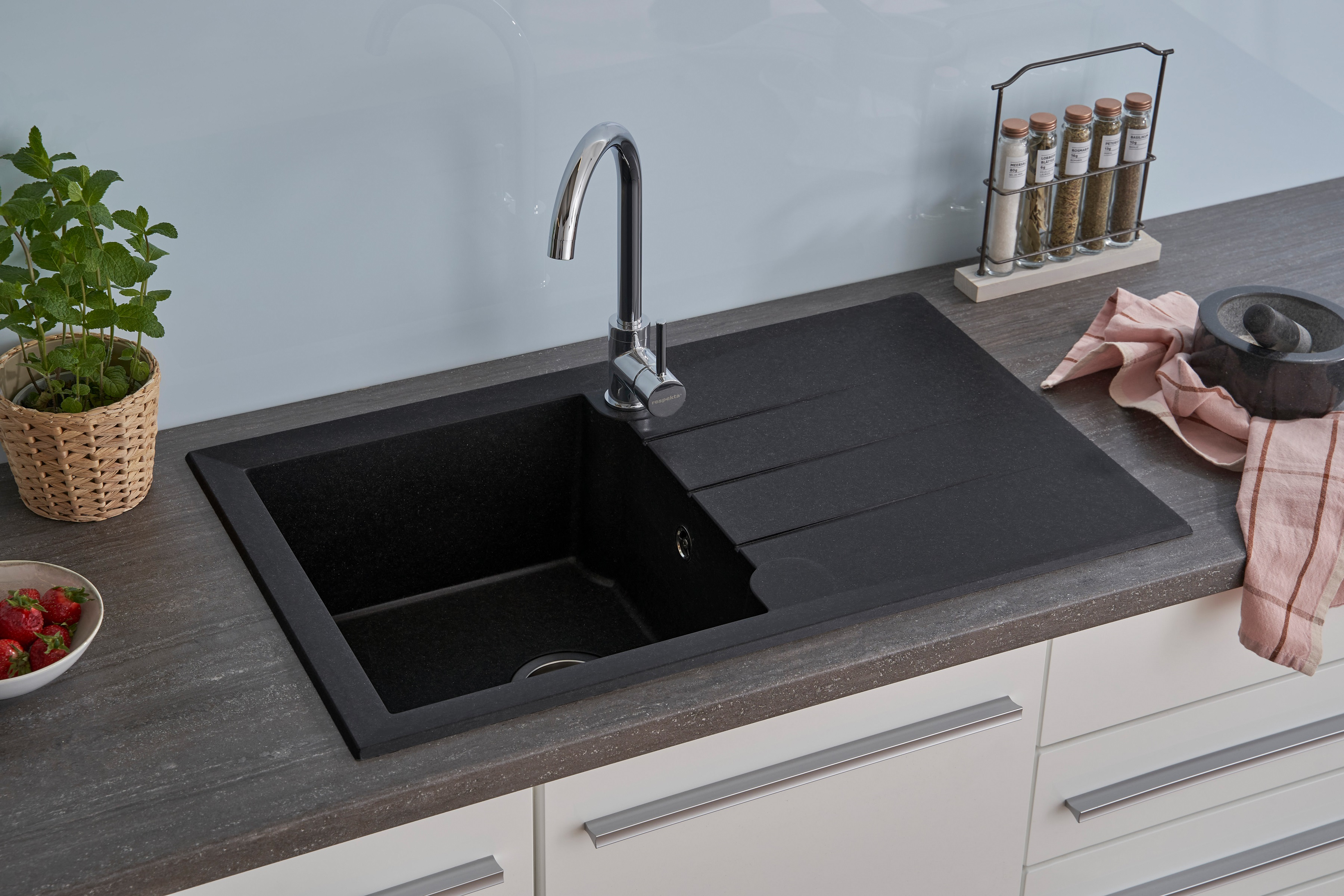Ein schwarzes Küchenbecken mit schwarzer Arbeitsplatte, Wasserhahn und Fenster im Hintergrund.