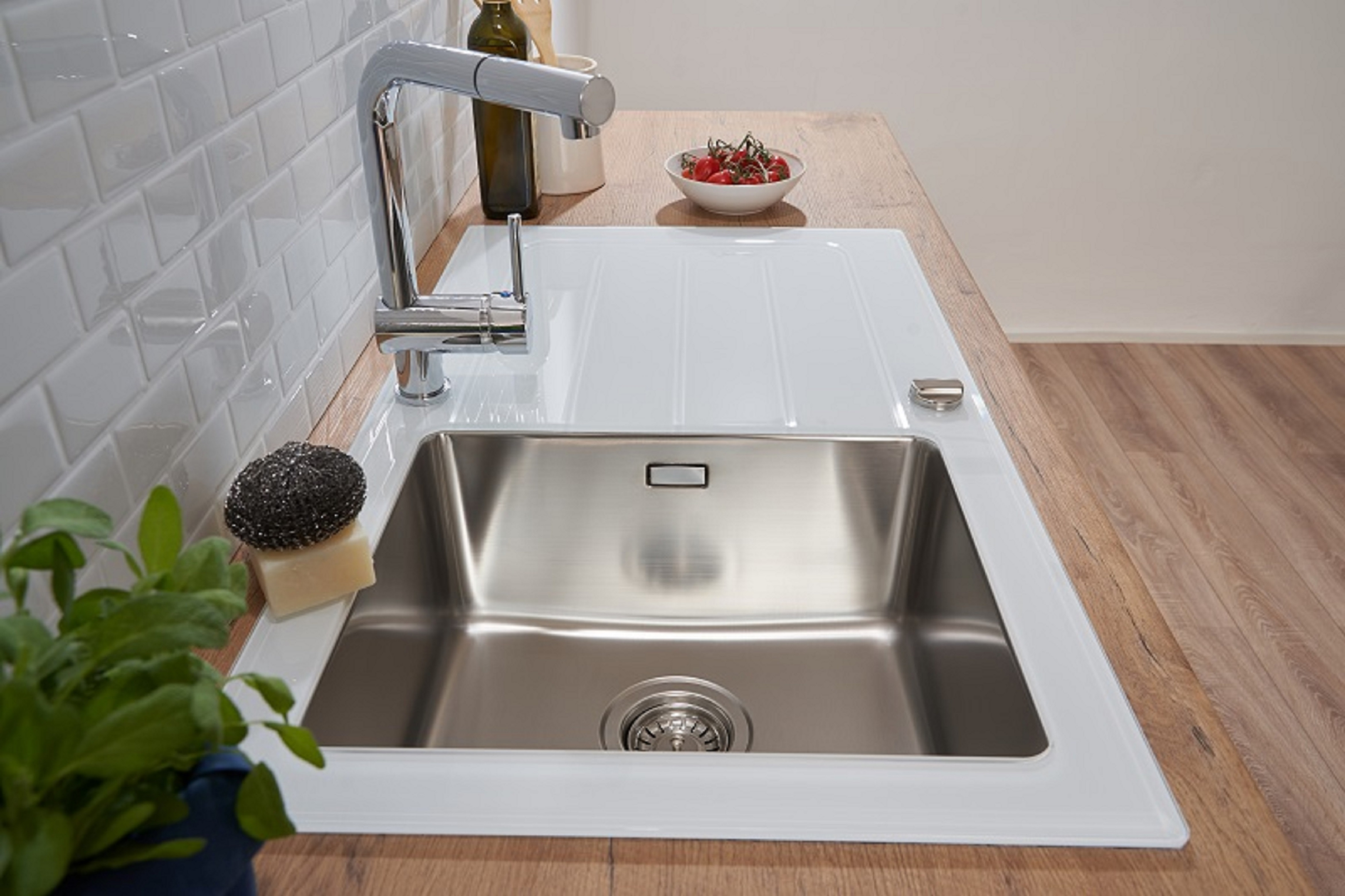 Ein Edelstahlspülbecken mit Wasserhahn. Ein Schwamm und Seife auf der Theke. Eine Schüssel mit Tomaten.
