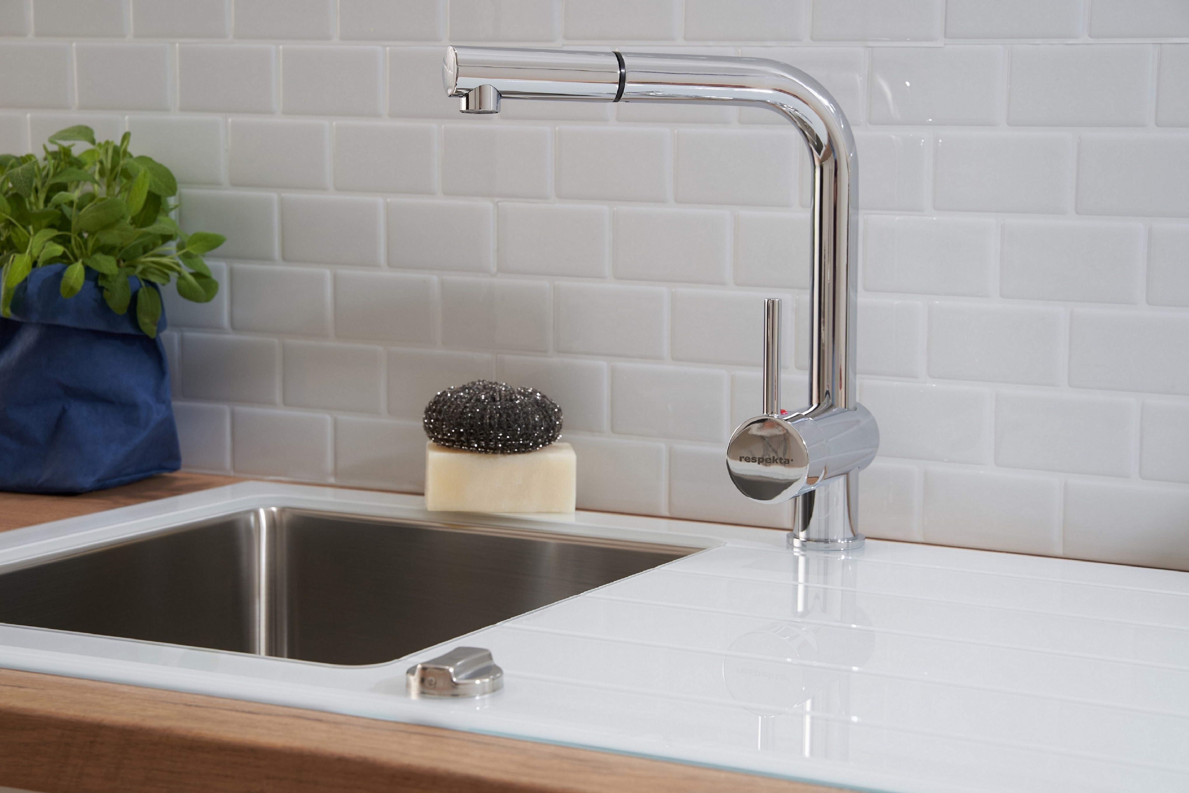 Chromarmatur über einem weißen Waschbecken mit weißer Arbeitsplatte und weißer Fliese.