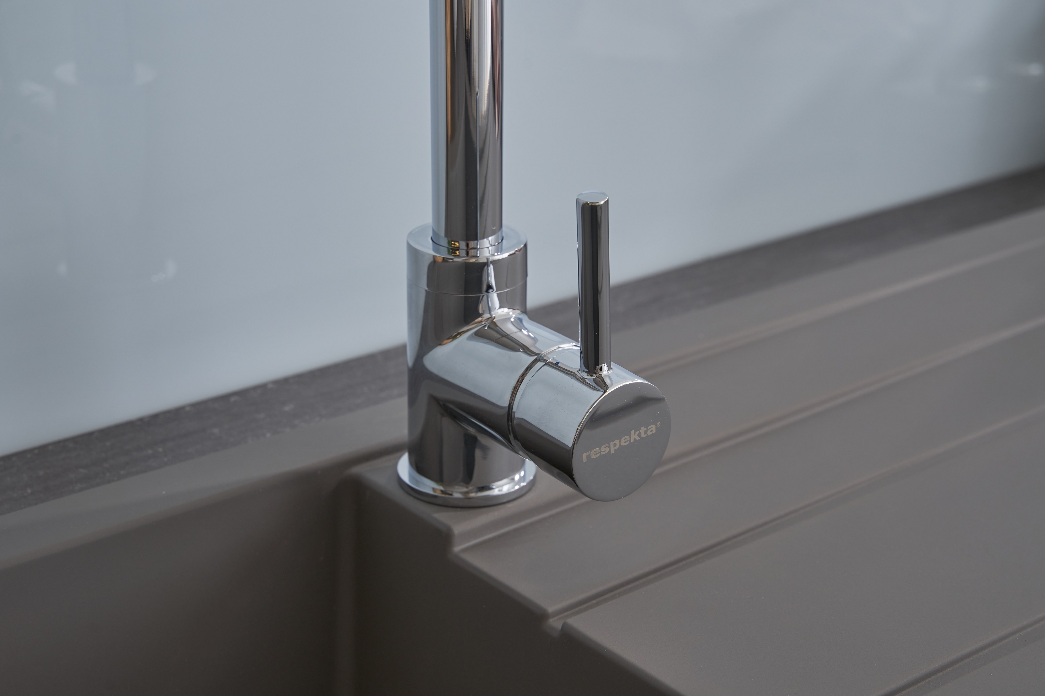 Chrom-Wasserhahn auf einem grauen Waschbecken. Nahaufnahme einer modernen Küchenarmatur. Heller Hintergrund.