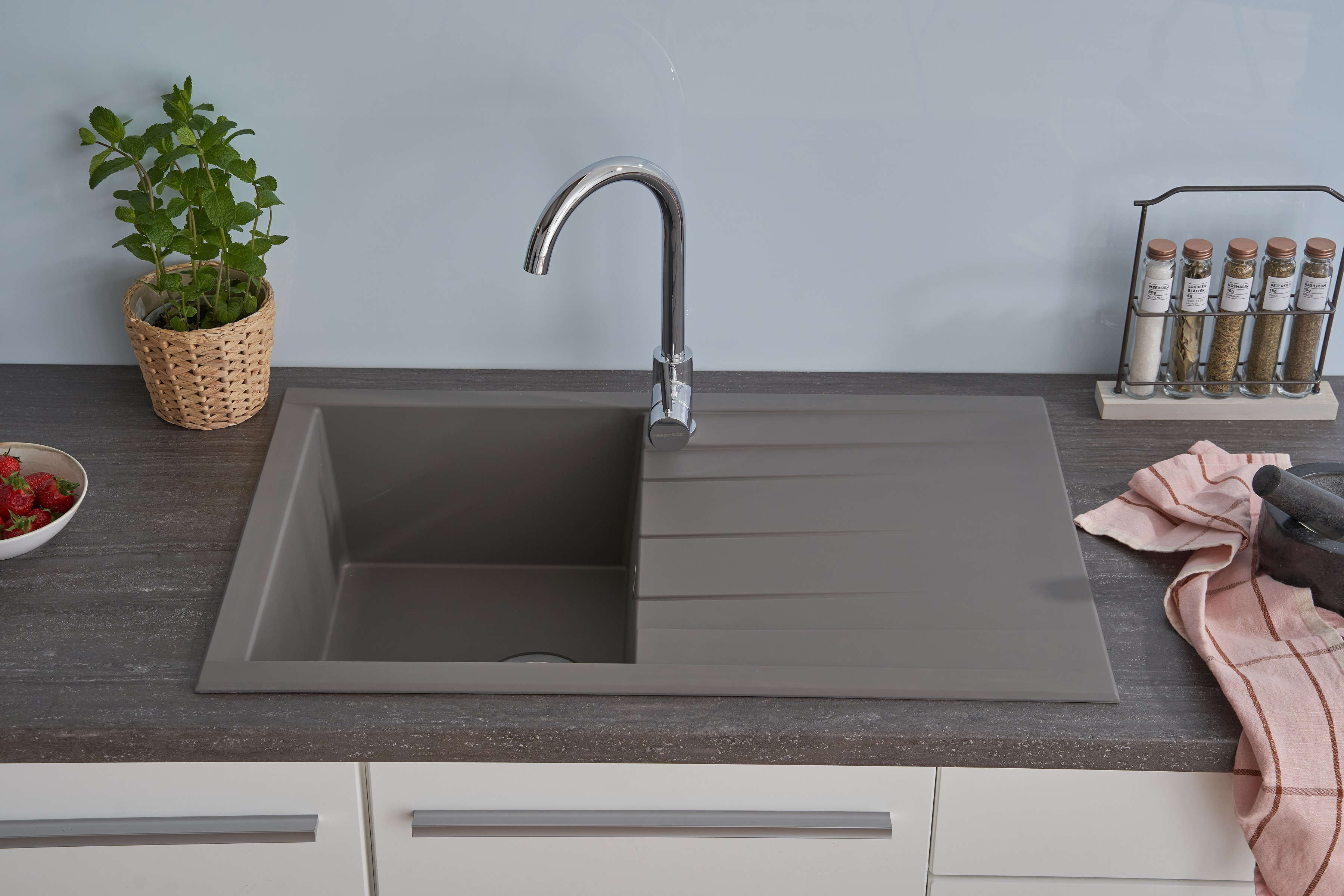 Küchenspüle mit Wasserhahn, eingebaut in eine Arbeitsplatte mit Erdbeeren und Gewürzgläsern.