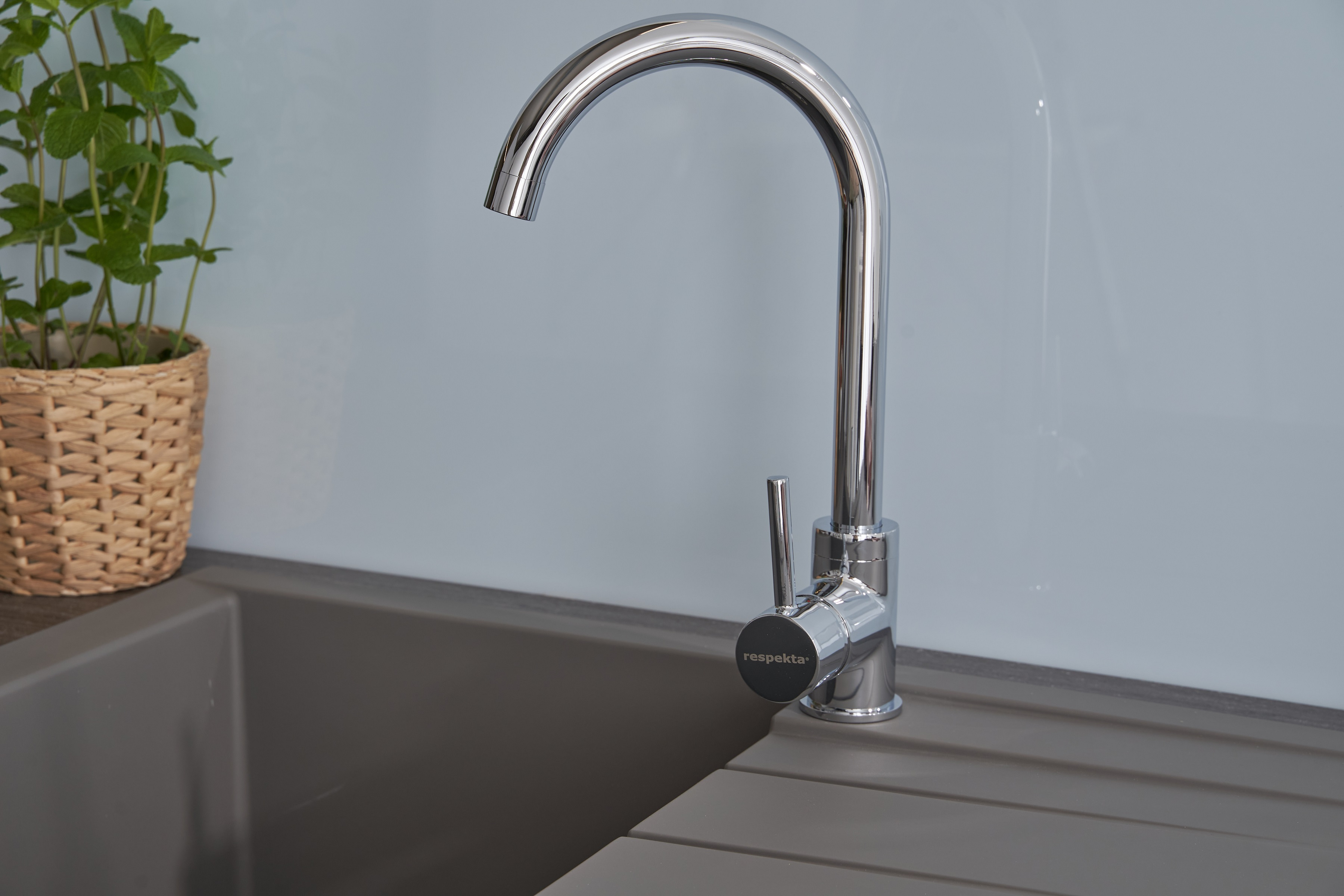 Chrom-Küchenarmatur über einem grauen Waschbecken, neben einer Pflanze in einem Weidenkorb auf der Theke.