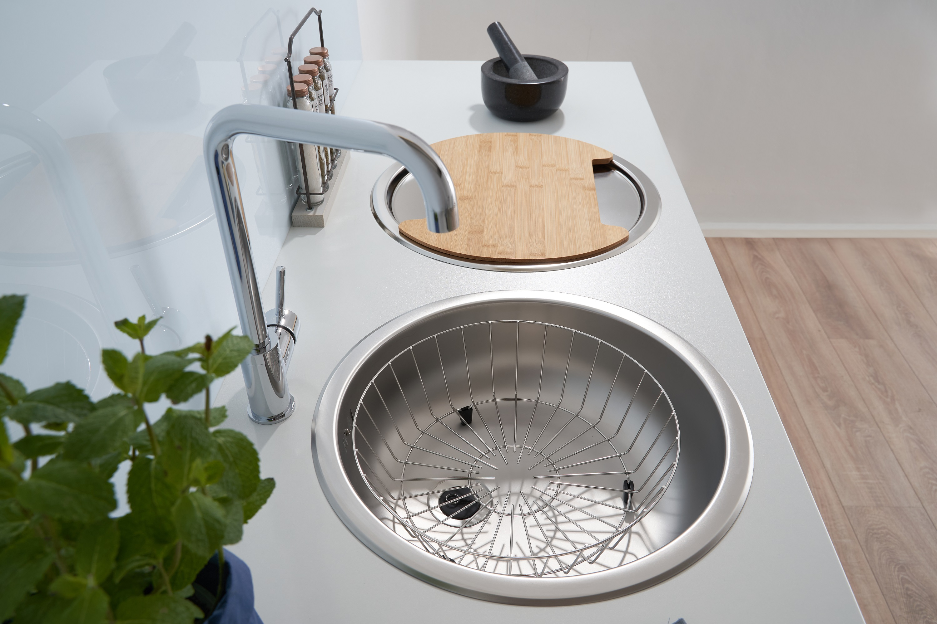 Moderne Küchenspüle mit Wasserhahn, rundem Waschbecken mit Drahtkorb und Holzschneidebrett.