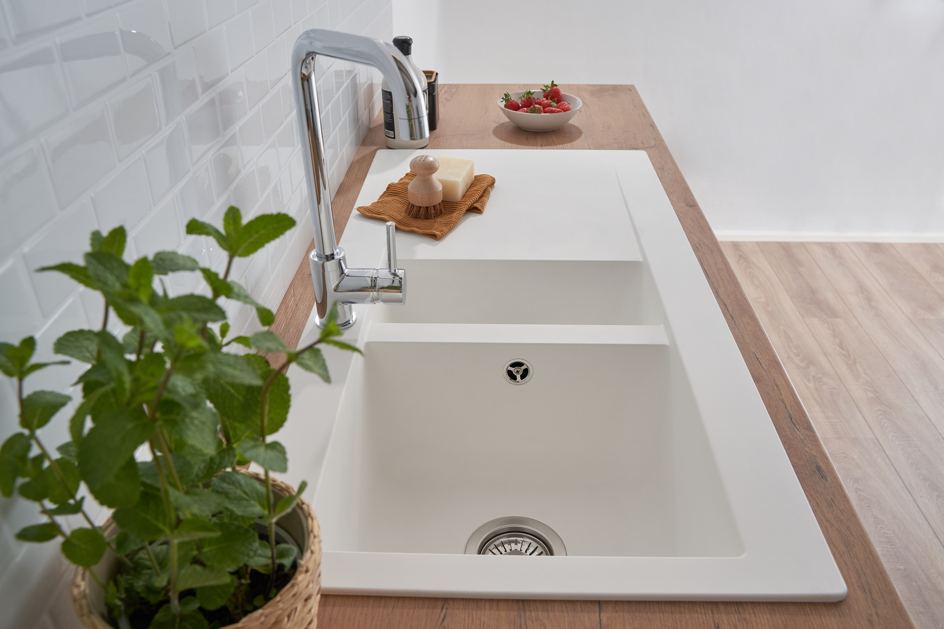 Weißes Küchenbecken mit Wasserhahn und Holz-Arbeitsplatte. Eine Pflanze und Erdbeeren sind zu sehen.