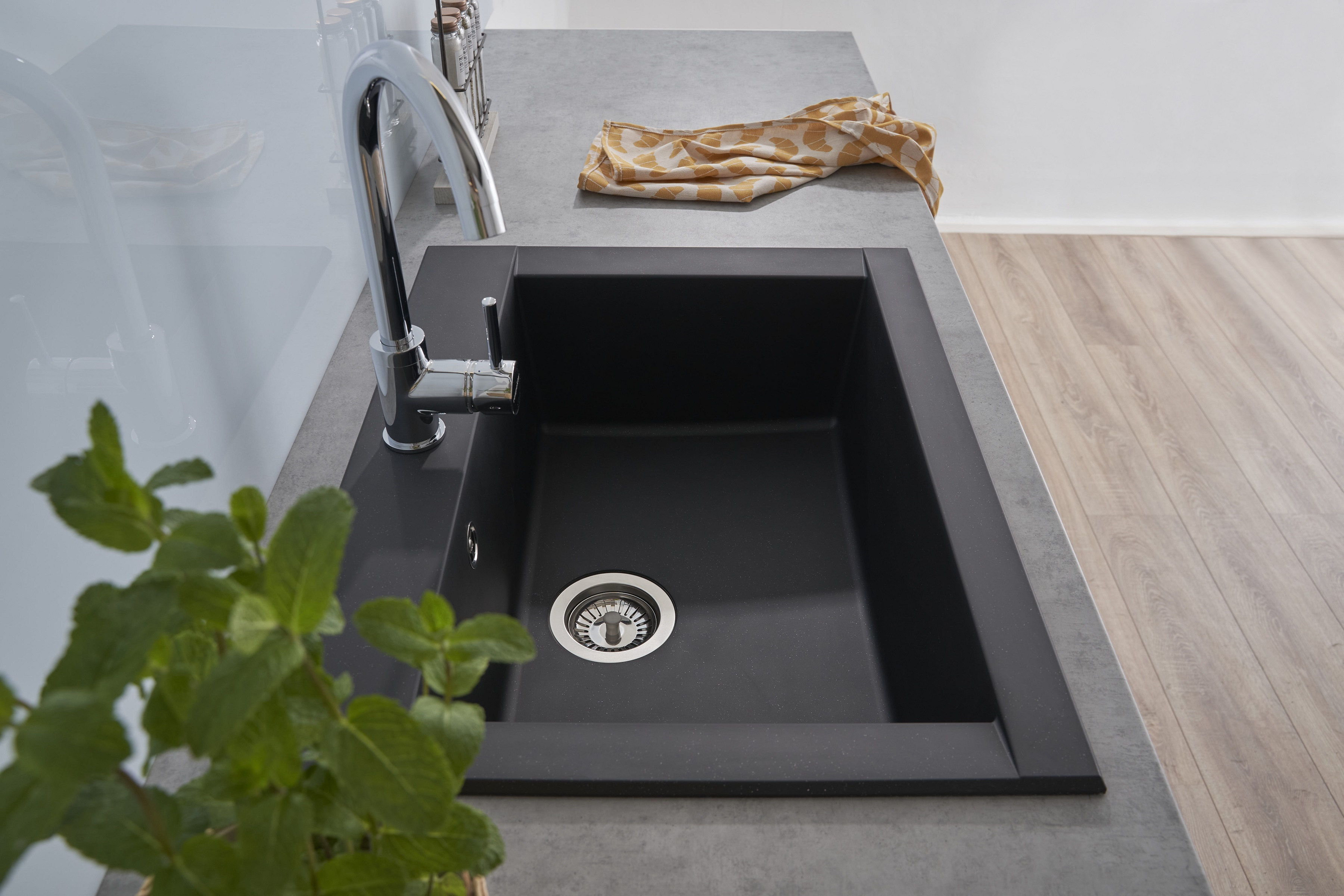 Ein schwarzes Küchenbecken in einer grauen Arbeitsplatte, mit Chromarmatur, Seife und einer Pflanze.
