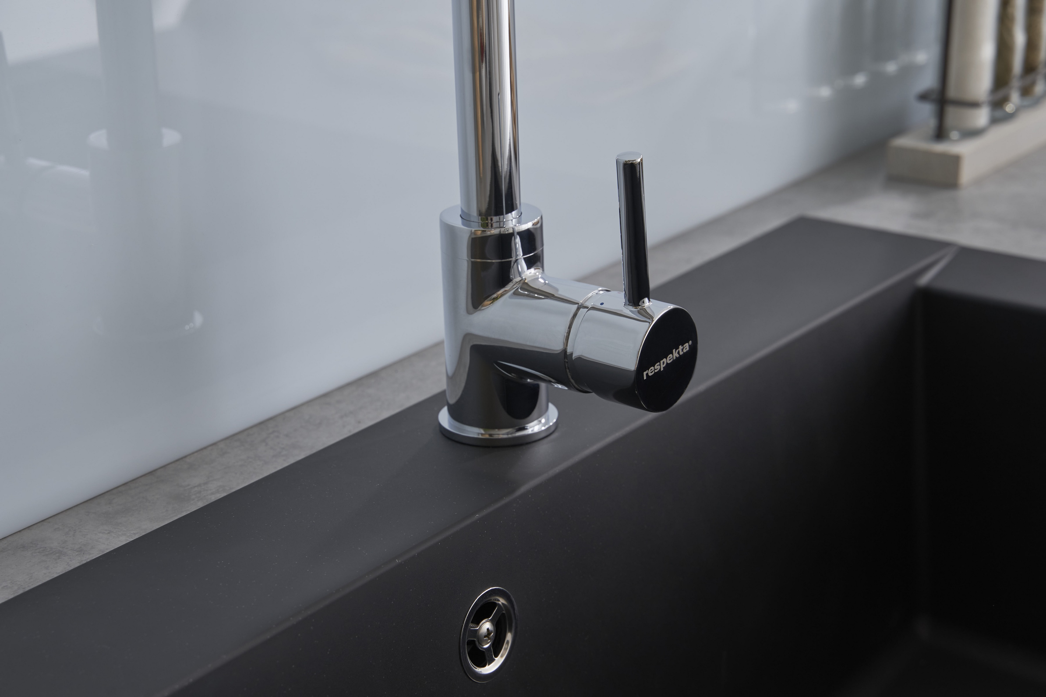 Chromarmatur über einem schwarzen Waschbecken, Nahaufnahme, vor weißem Hintergrund.