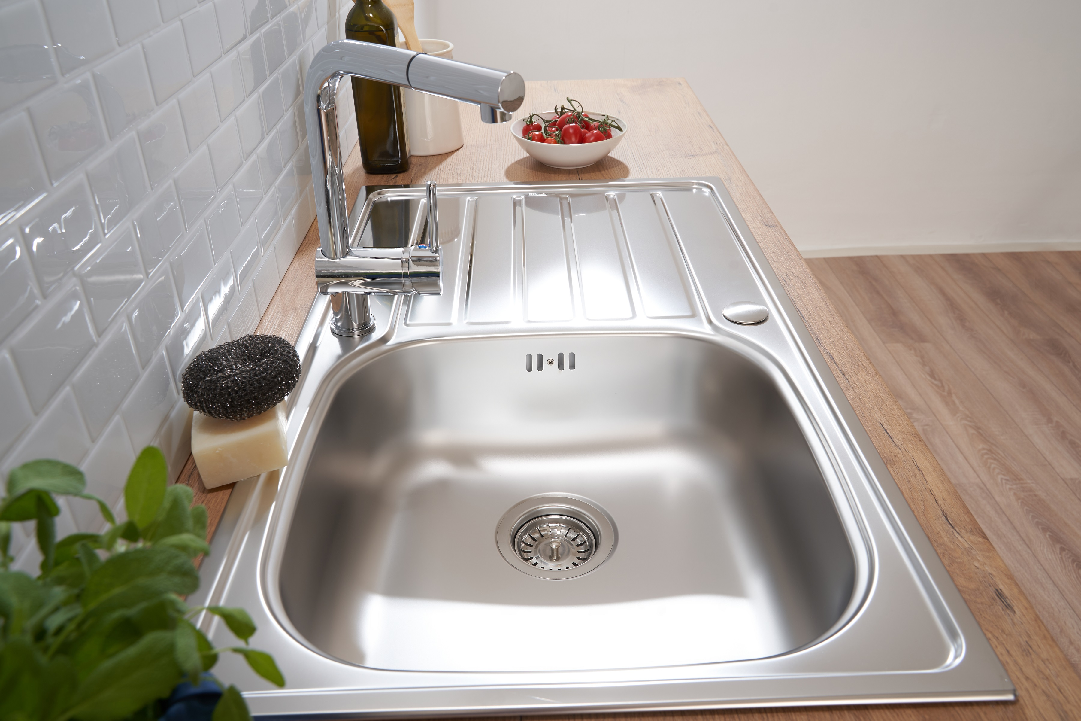 Edelstahl-Küchenspüle mit Wasserhahn, Seife, Schwamm und Tomaten.