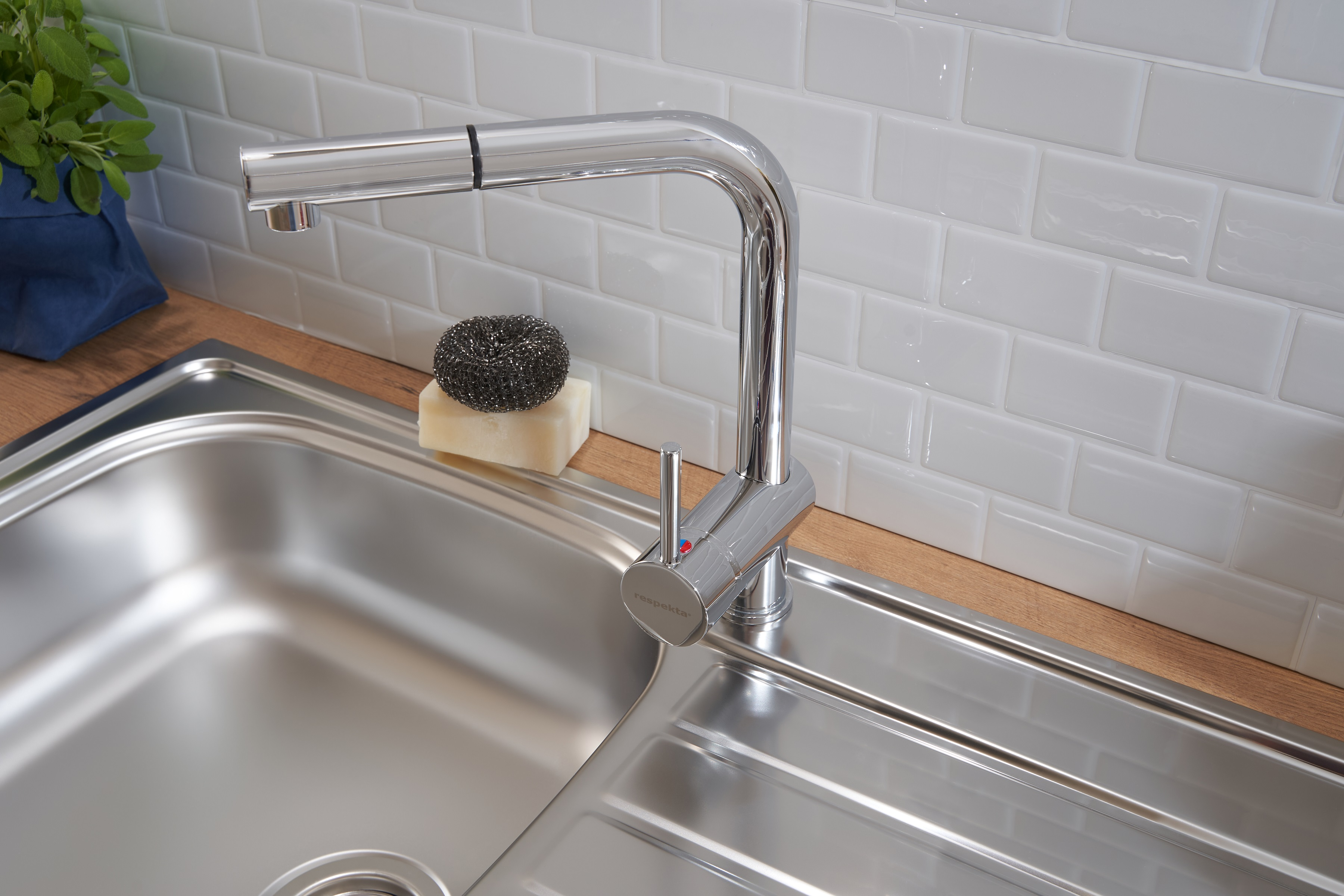 Edelstahl-Küchenspüle mit Chromarmatur, Schwamm und Kachelhintergrund.
