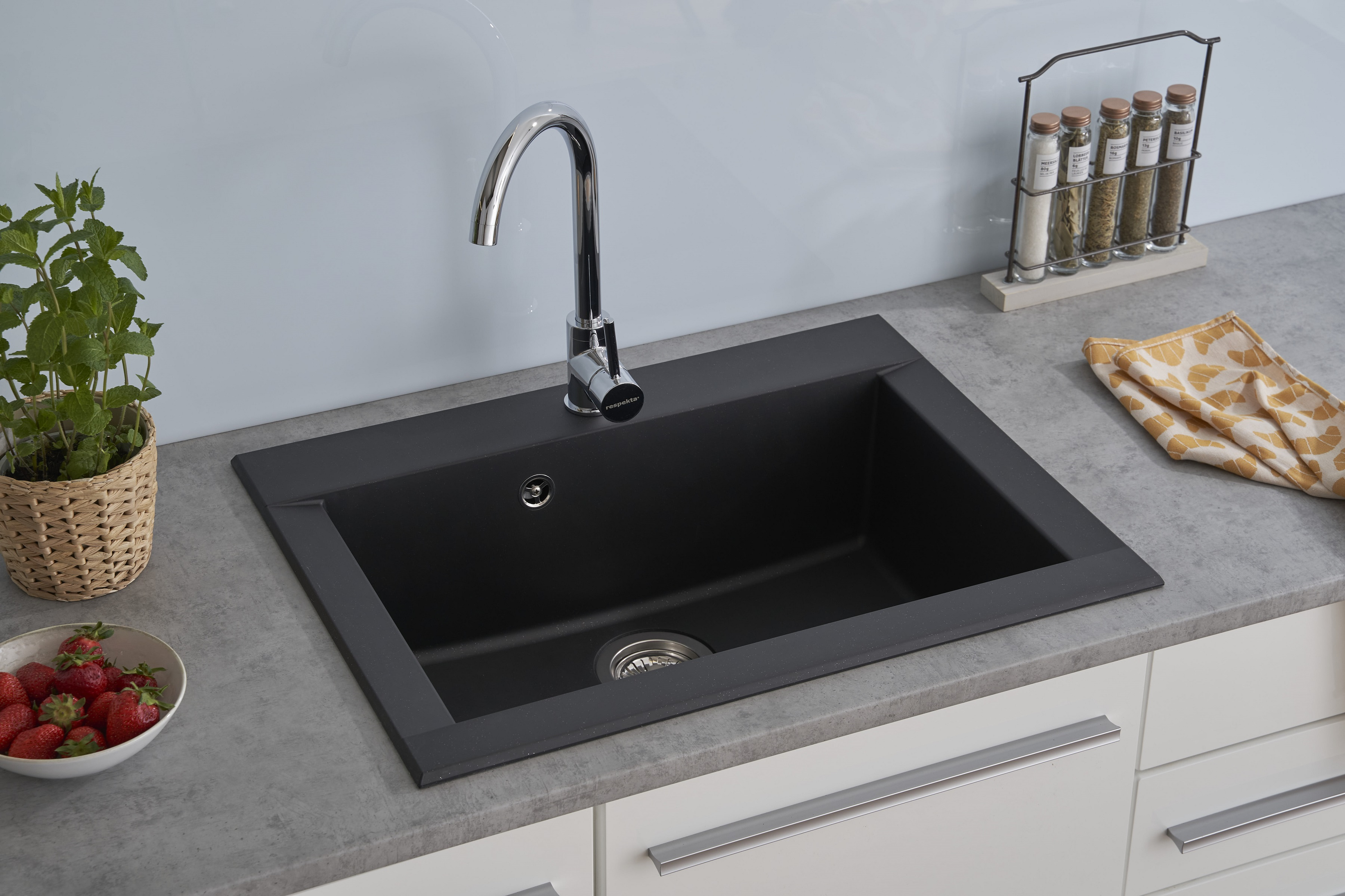 Schwarzes Waschbecken mit Chromarmatur, Erdbeeren in einer Schüssel, Gewürze und ein Küchentuch.