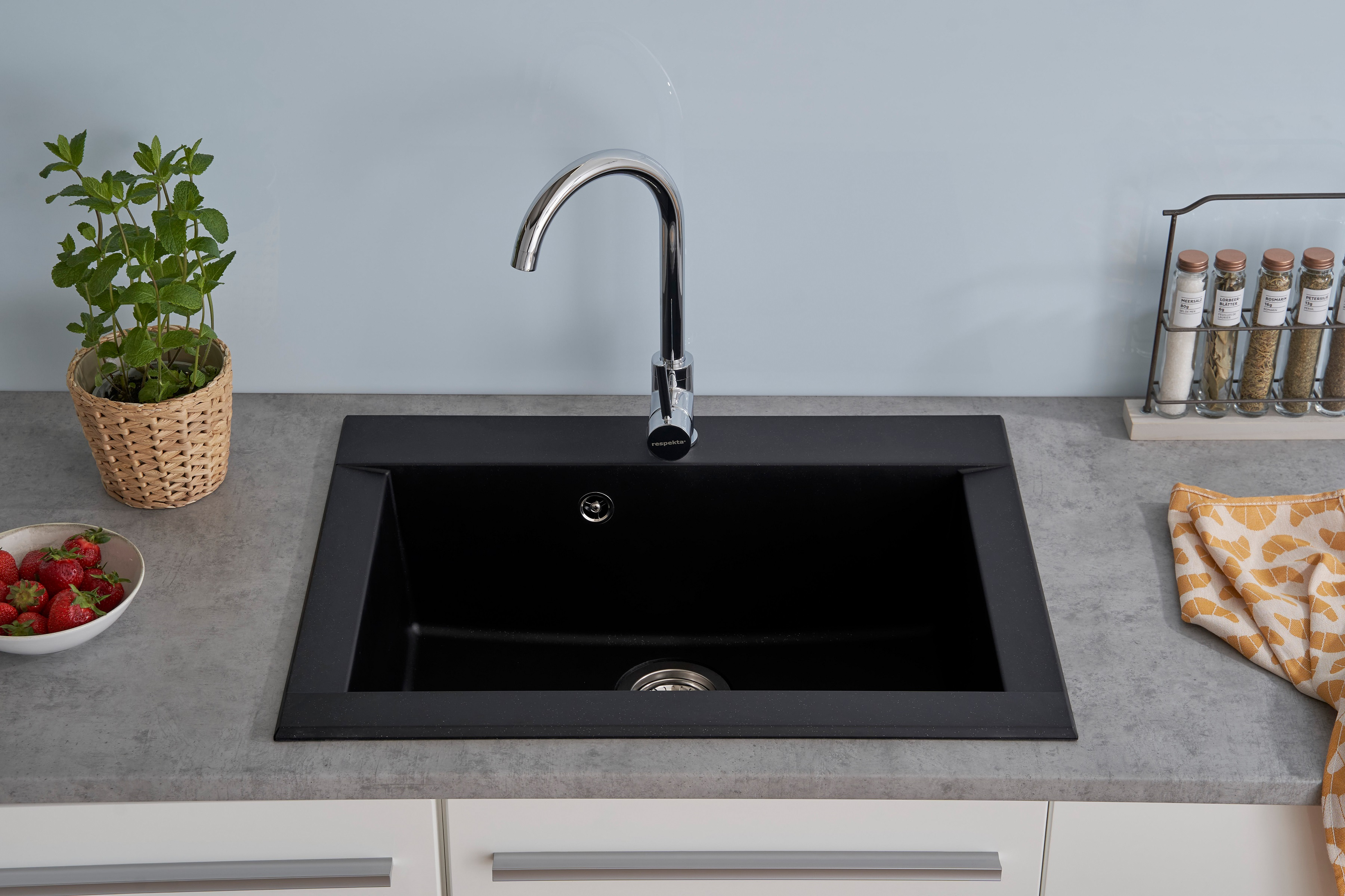 Schwarzes Küchenbecken mit Chromarmatur, mit Erdbeeren, Minze und Gewürzen.