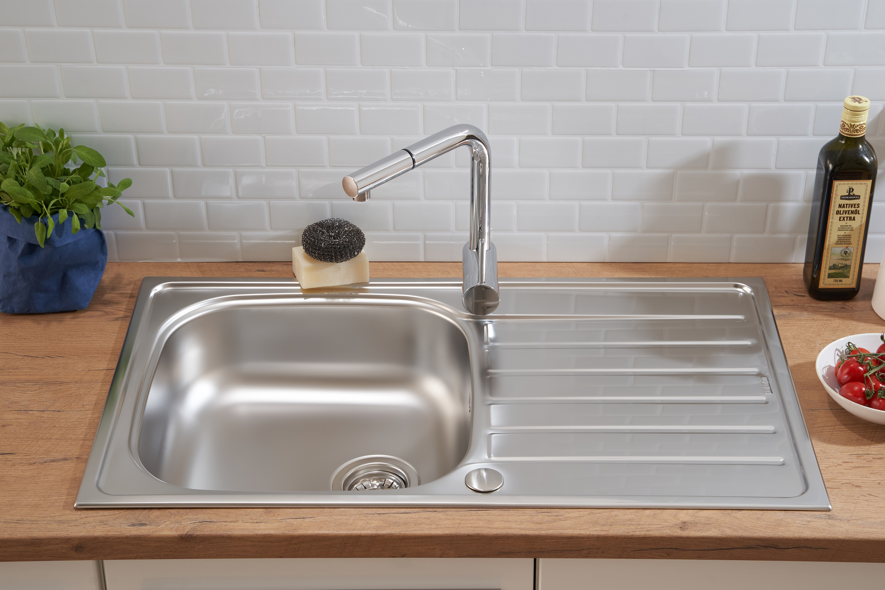 Ein Edelstahlspülbecken mit Wasserhahn auf einer Holz-Arbeitsplatte mit weißem Fliesen-Hintergrund.