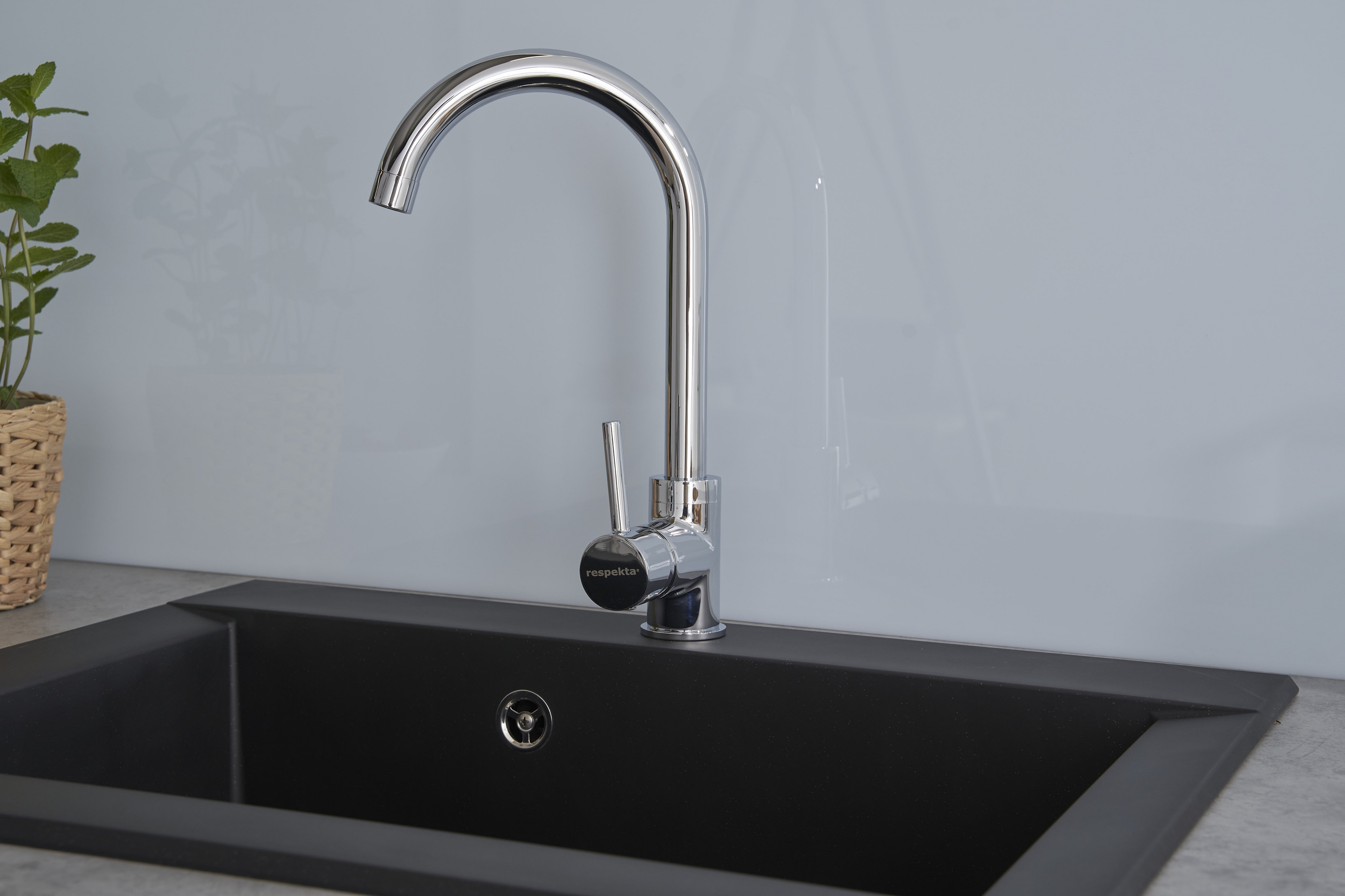 Ein verchromter Wasserhahn über einem schwarzen Waschbecken. Der Wasserhahn ist gebogen und das Waschbecken hat ein schlankes, modernes Design.