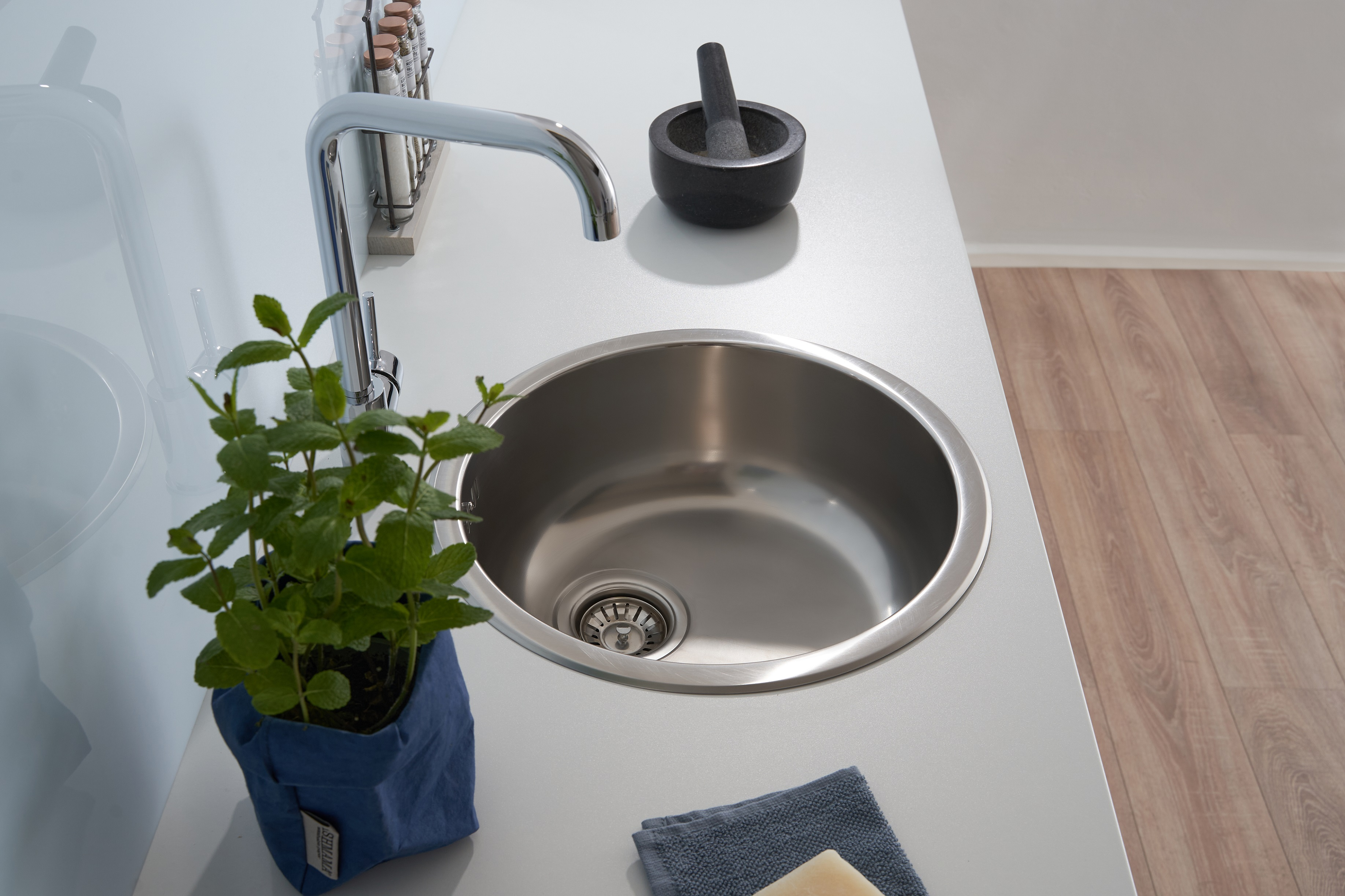 Küchenspüle mit Wasserhahn, Pflanze und Mörser.