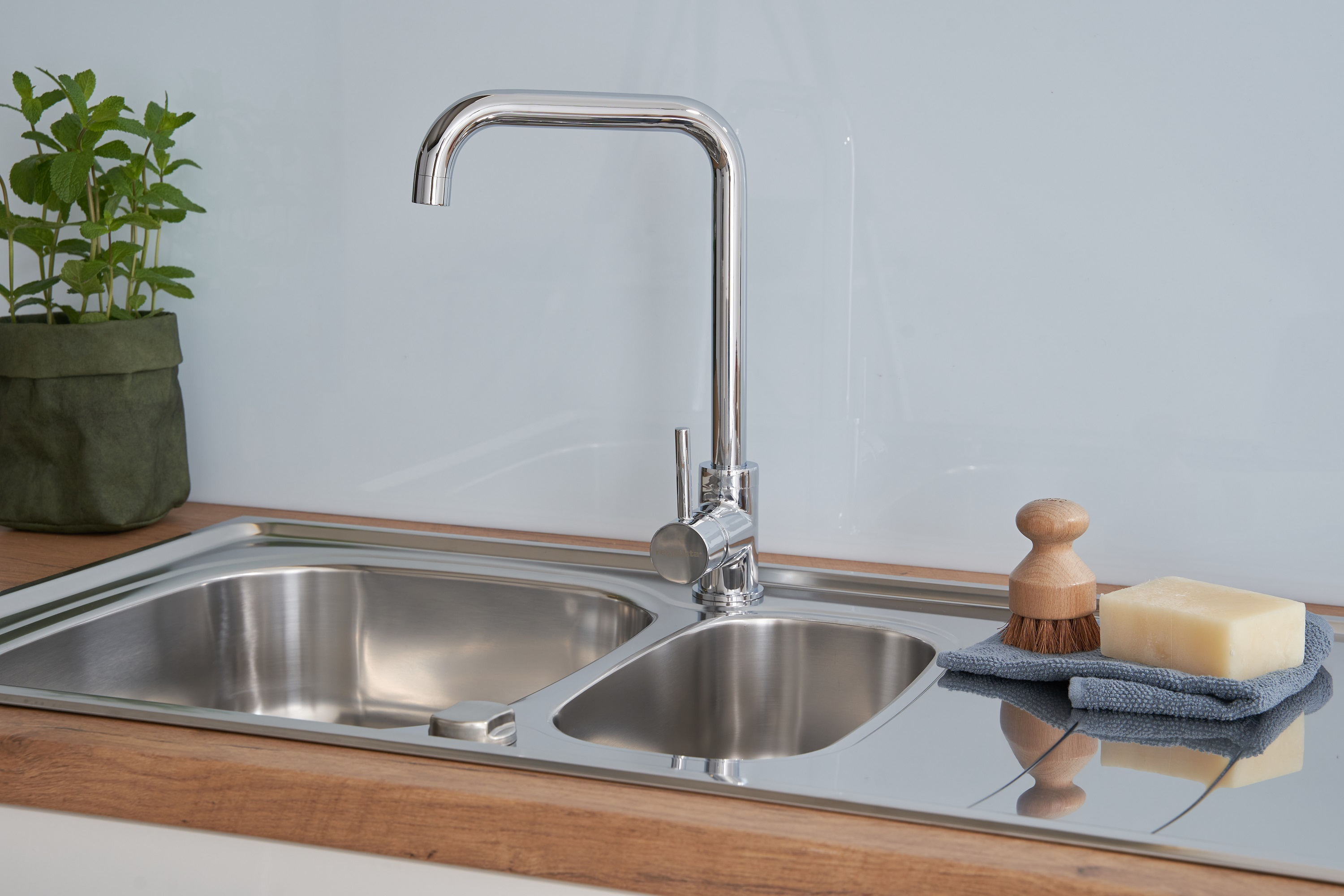Edelstahl-Küchenspüle mit Wasserhahn und Seife. Minzpflanze in einer grünen Tüte.