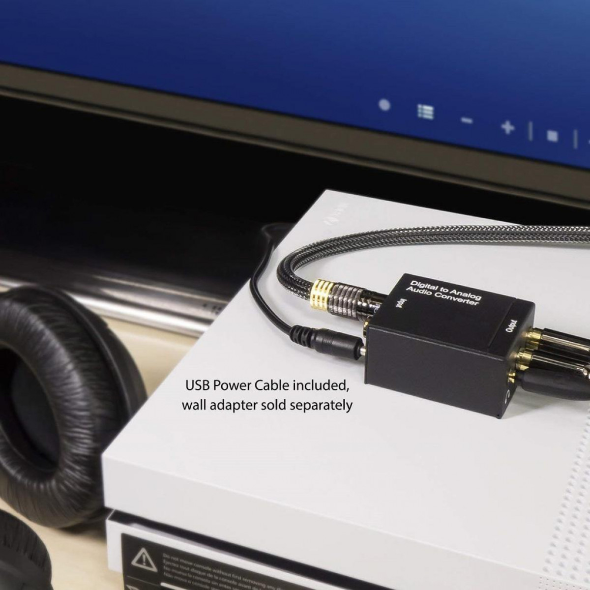 Czarny konwerter audio cyfrowo-analogowy z kablami na białej powierzchni. Słuchawki i ekran w tle.