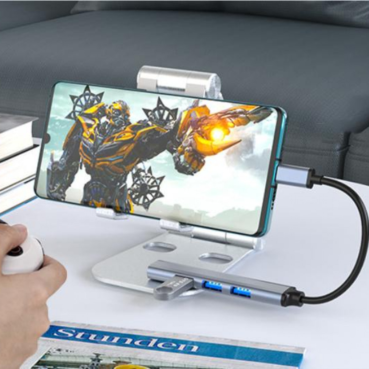 Telefon auf Ständer mit Film. USB-Hub verbunden. Hand hält Gamecontroller.