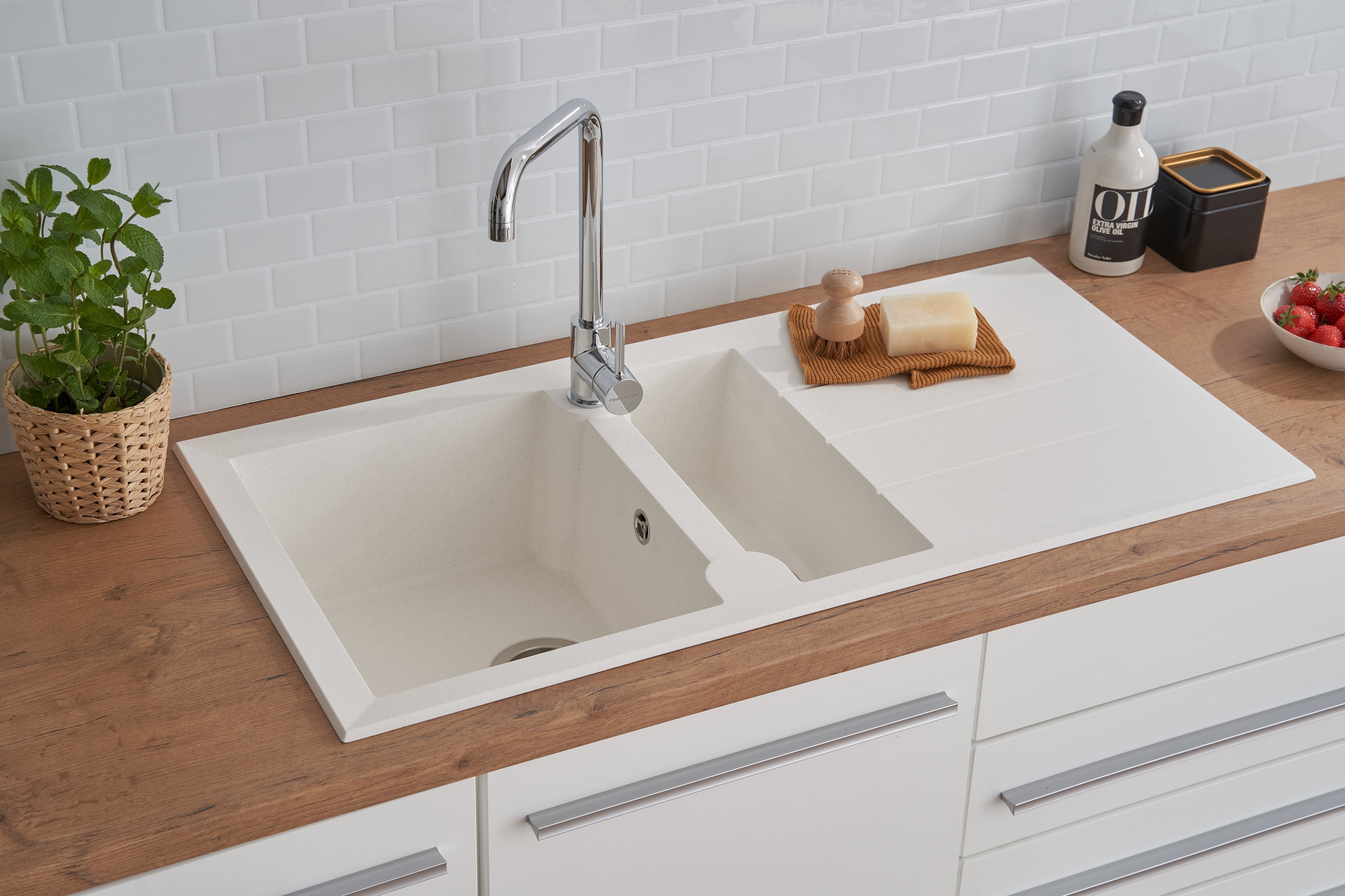 Weißes Küchenbecken mit Wasserhahn, Seife und Pflanze. Holz-Arbeitsplatte.