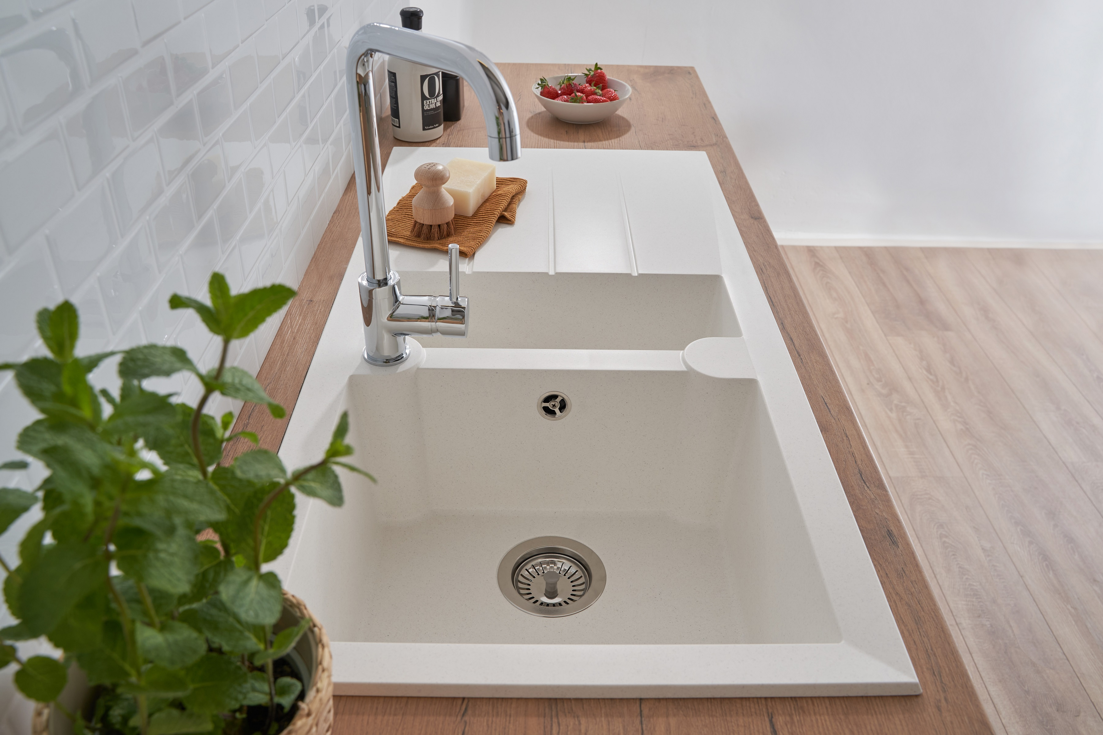 Ein Küchenspülbecken mit Chromarmatur. Erdbeeren und ein Holzbrett liegen auf der Theke. Weiße Wand dahinter.
