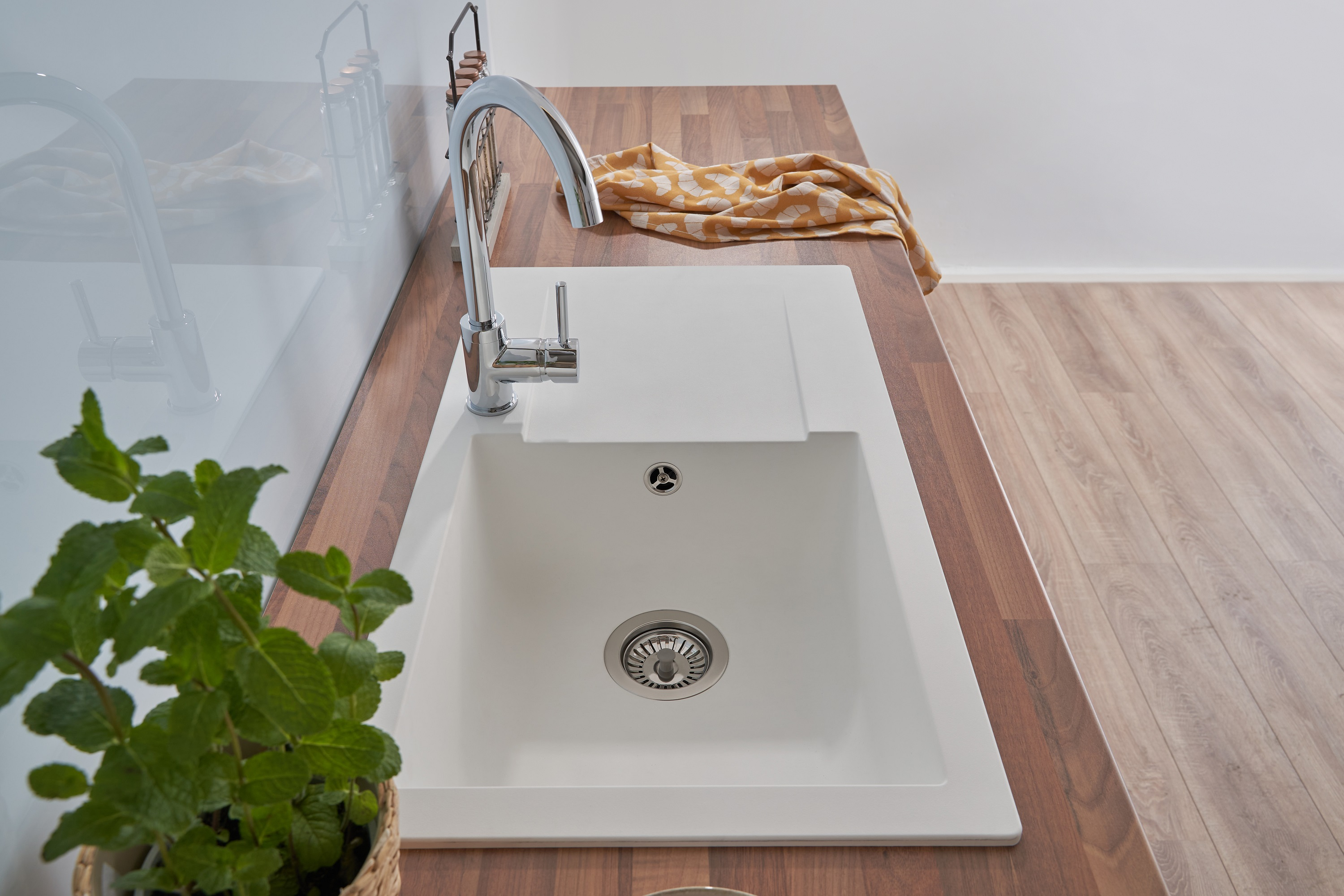 Küchenspüle mit Wasserhahn, Holzplatte. Minzepflanze im Korb links.