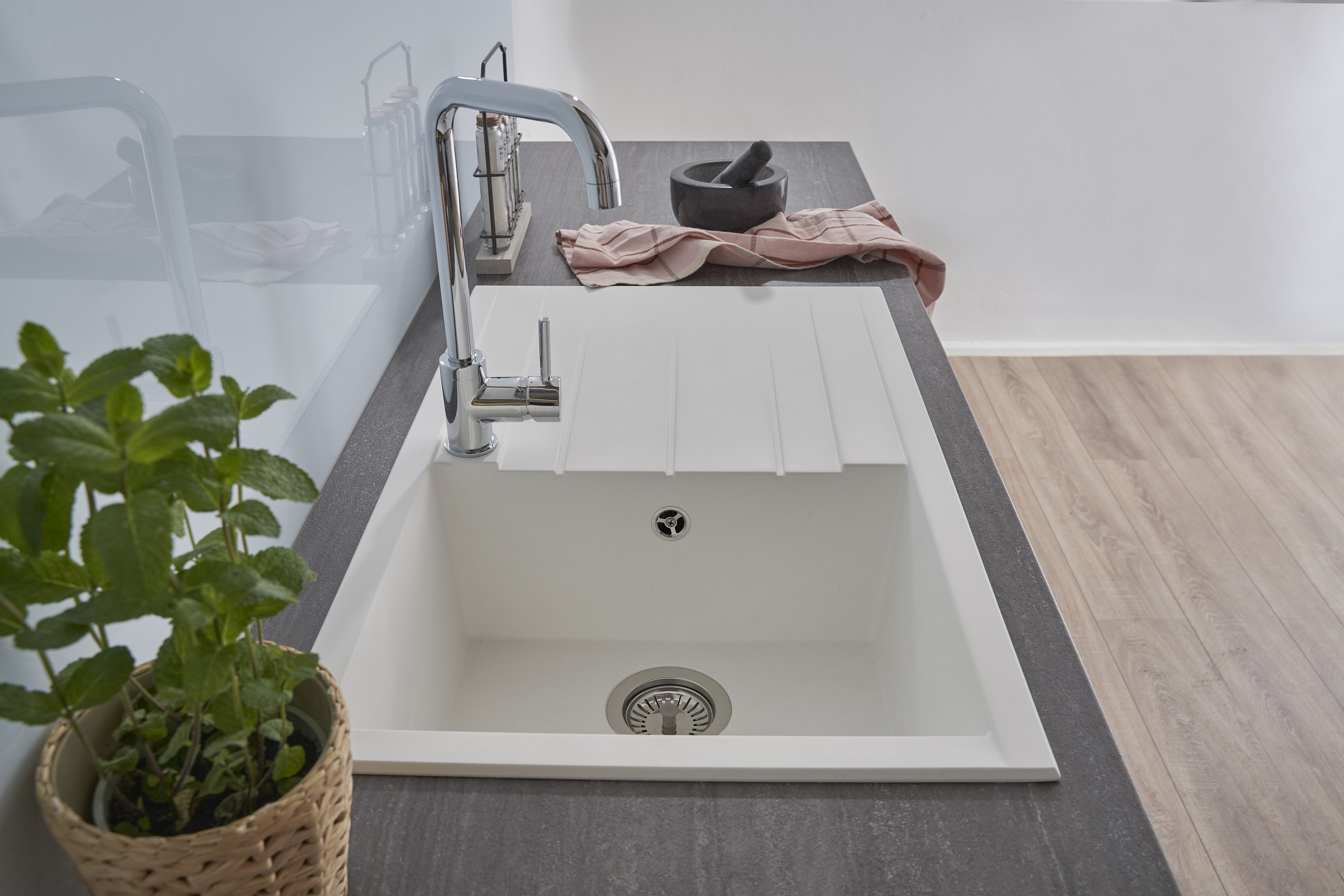 Weißes Küchenbecken mit Chromarmatur, einer Pflanze und einem rosa Tuch.