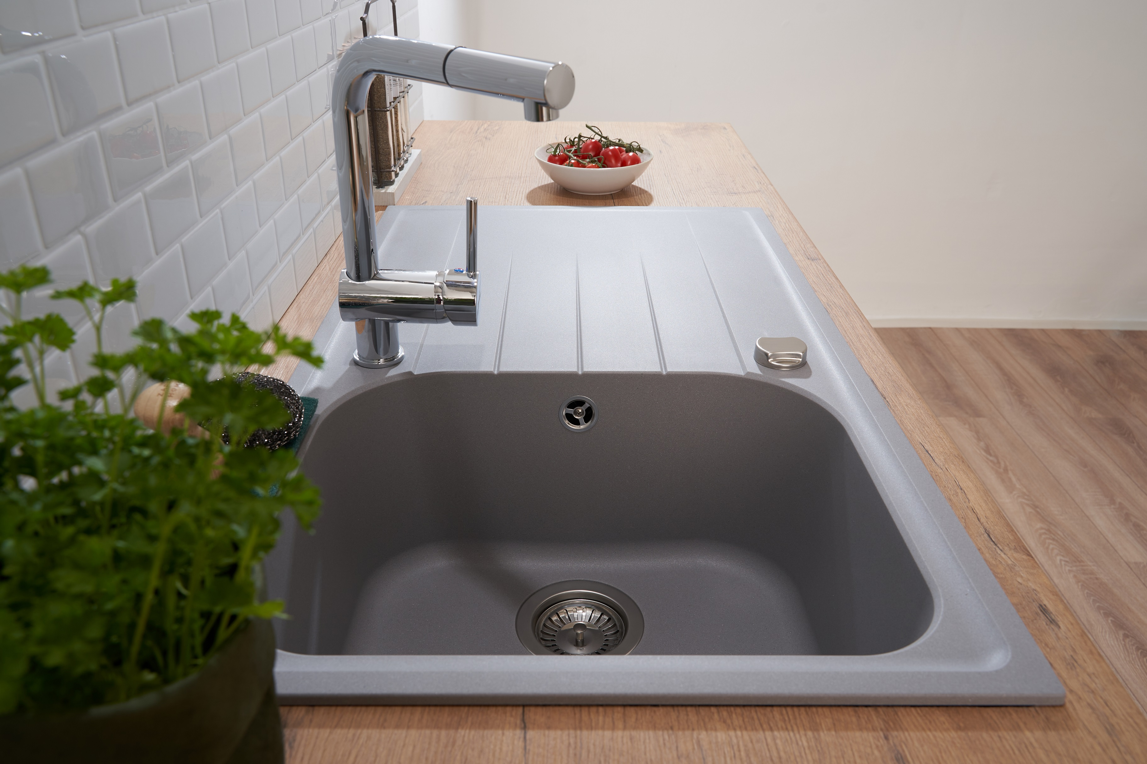 Ein graues Küchenbecken mit Wasserhahn, eine Schüssel mit Tomaten und eine Topfpflanze.