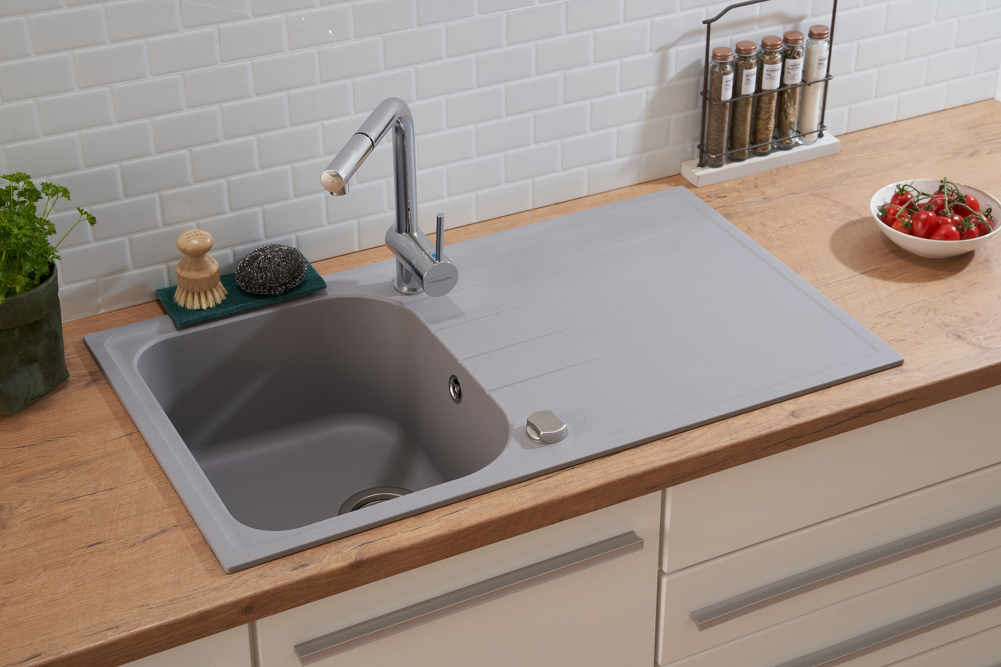Küchenspüle mit grauem Becken, Wasserhahn und Holzplatte. Tomaten und Bürste liegen daneben.