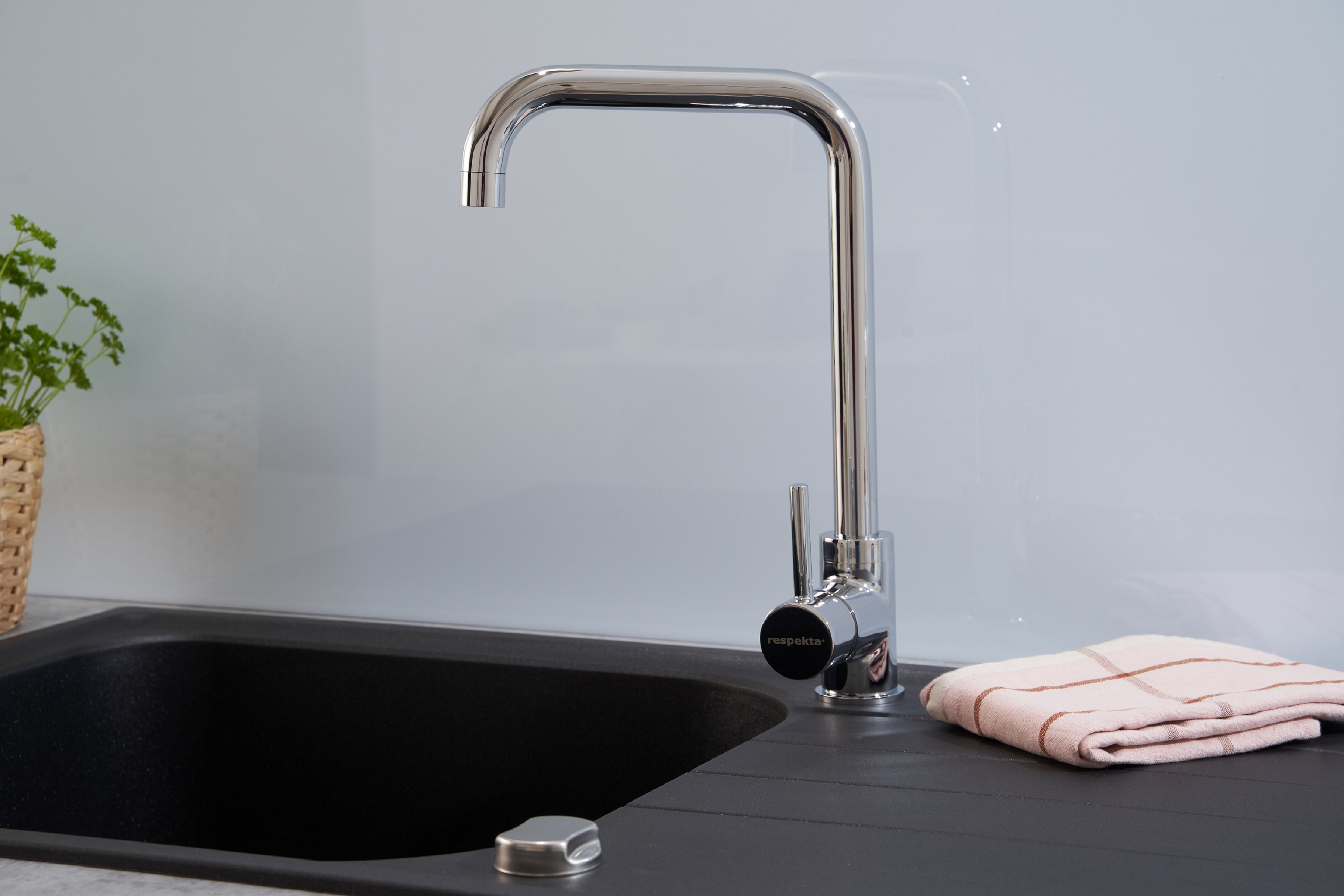 Eine glänzende Chrom-Küchenarmatur mit einem schwarzen Waschbecken und einem Handtuch auf der Theke.