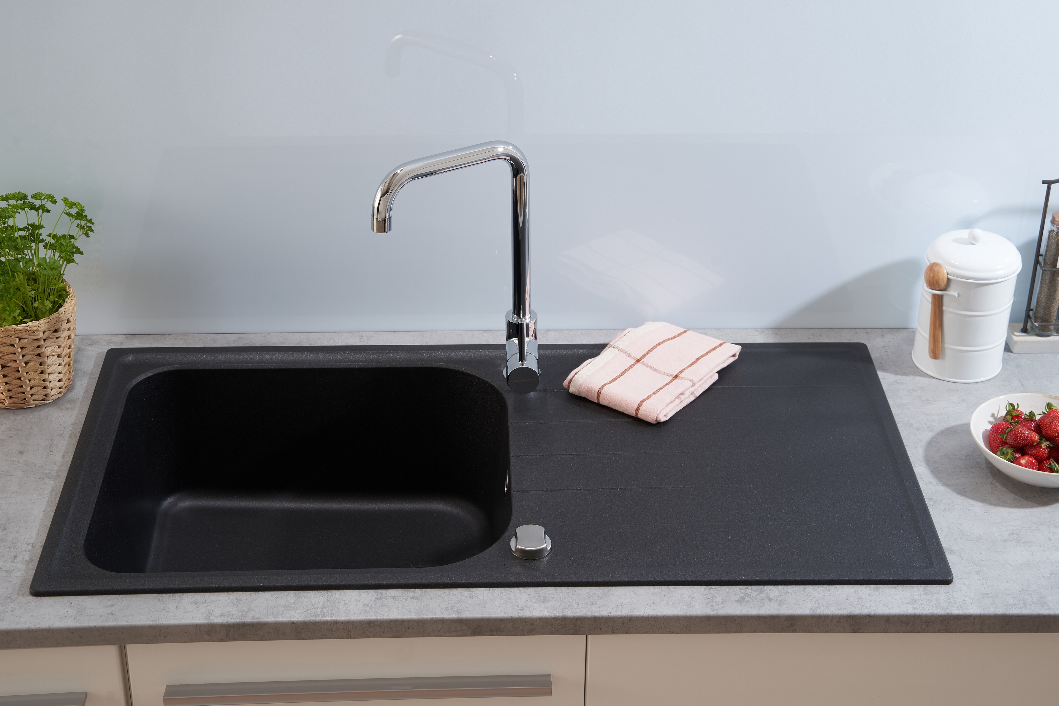 Schwarzes Küchenbecken mit verchromtem Wasserhahn. Ein Handtuch und Erdbeeren liegen auf der Arbeitsplatte.