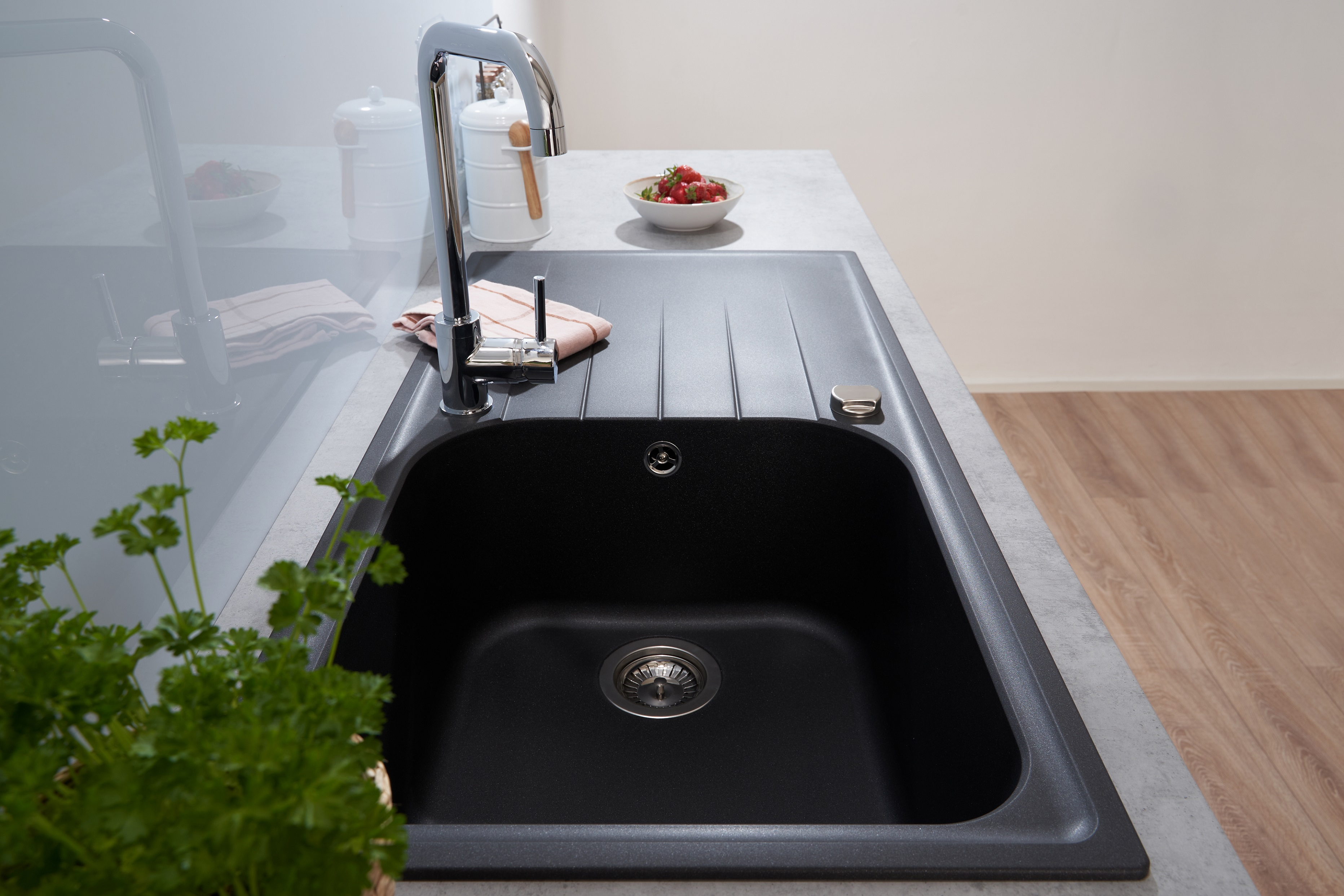 Schwarzes Küchenbecken mit Chromarmatur und weißer Arbeitsplatte. Petersilie und Erdbeeren.