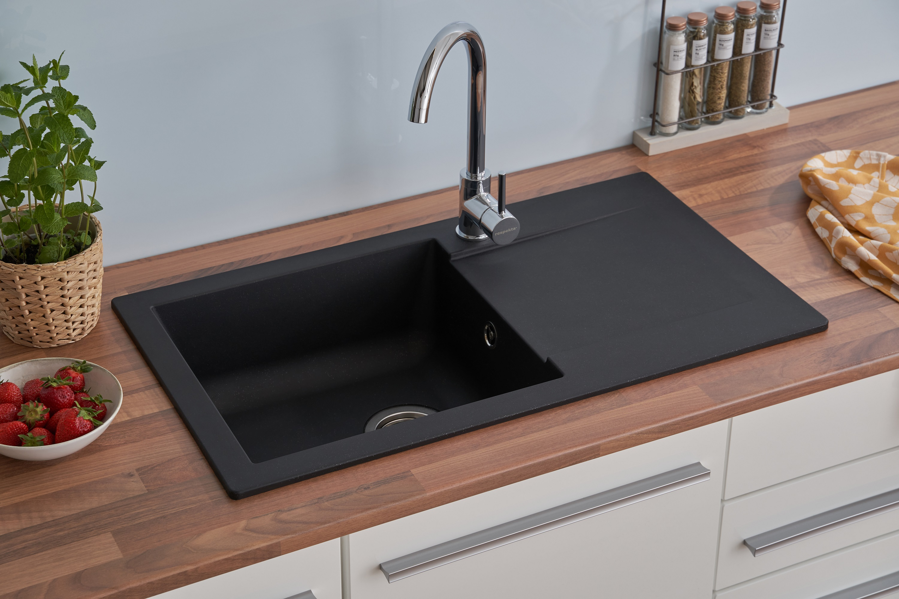 Küchenspüle mit Wasserhahn, Erdbeeren und Holz-Arbeitsplatte. Weiße Schränke.