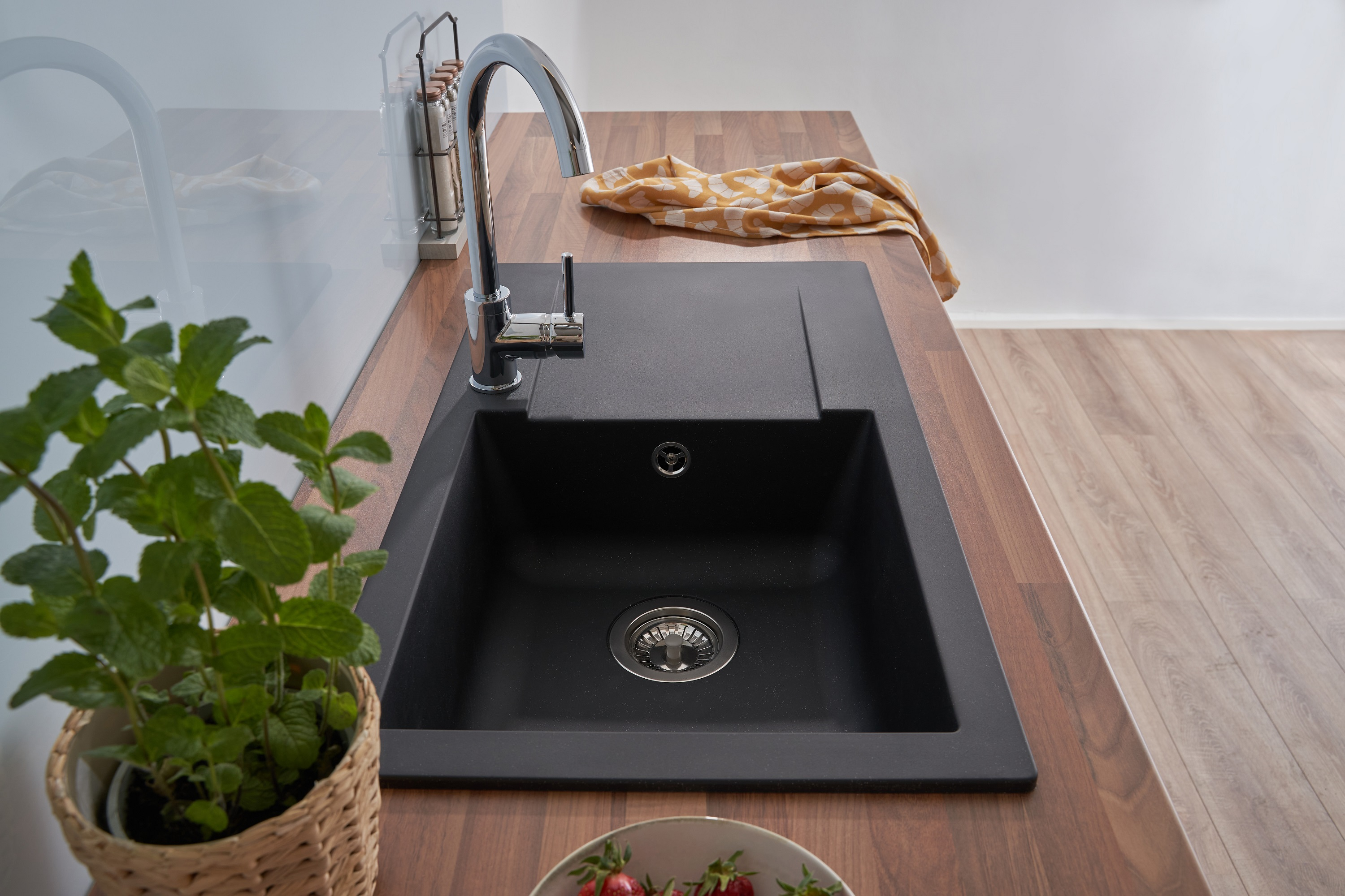 Ein schwarzes Waschbecken mit Chromarmatur in einer Küche. Eine Pflanze und ein gelbes Handtuch liegen auf der Holz-Arbeitsplatte.