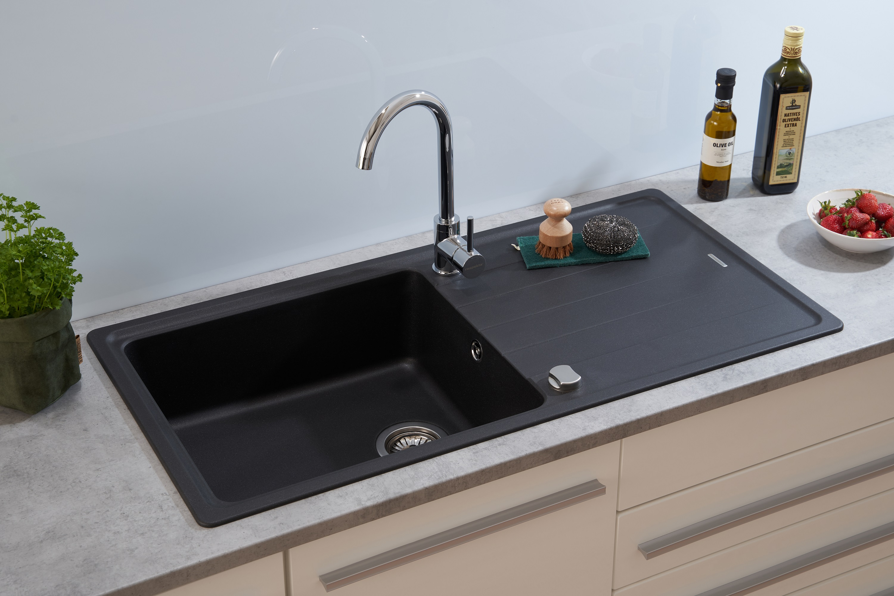 Schwarze Granit-Küchenspüle mit Wasserhahn, Abtropffläche und Zubehör auf der Arbeitsplatte.