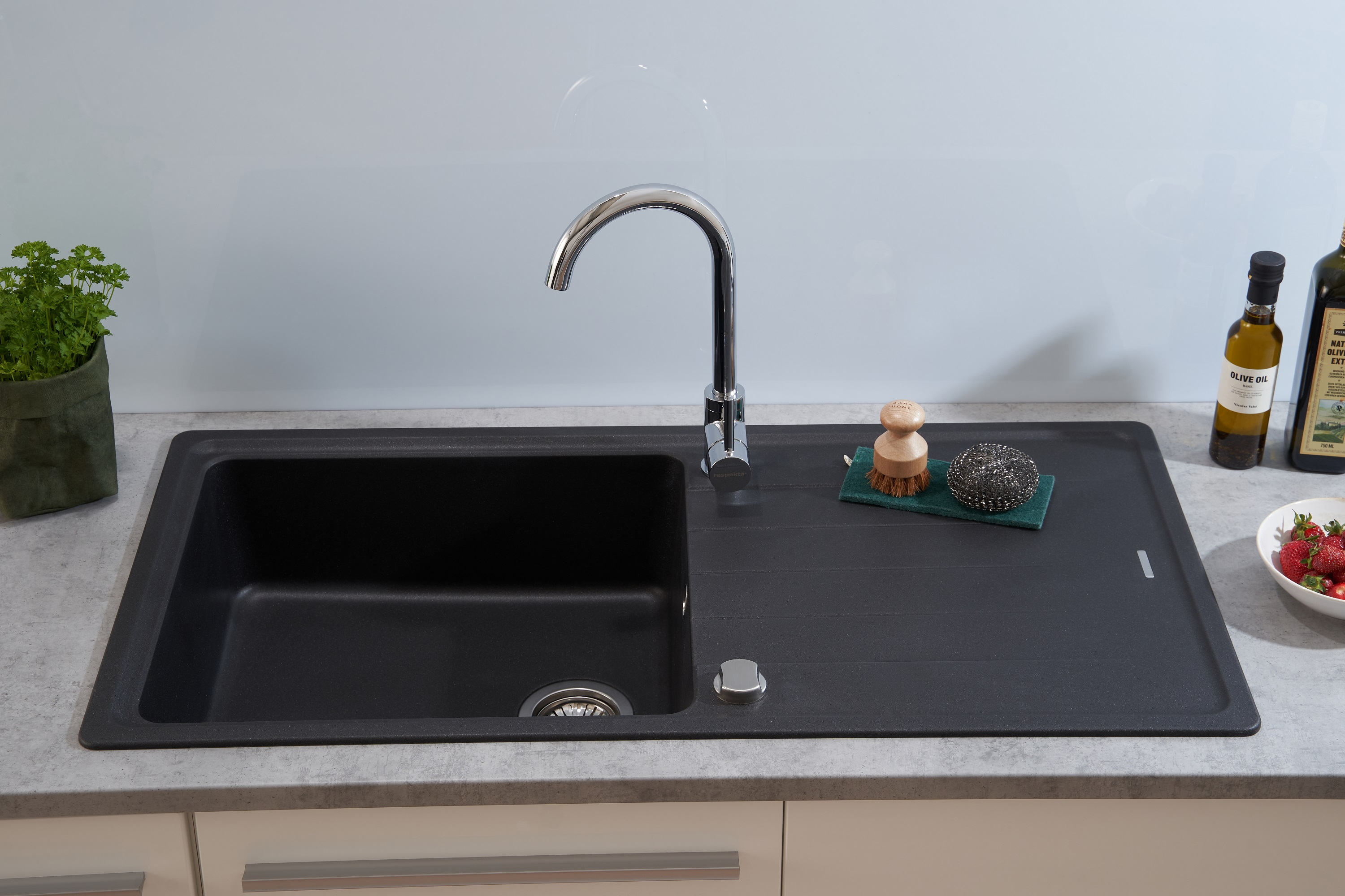 Schwarze Küchenspüle mit Wasserhahn, Schwamm und Erdbeeren, neben einer Pflanze.