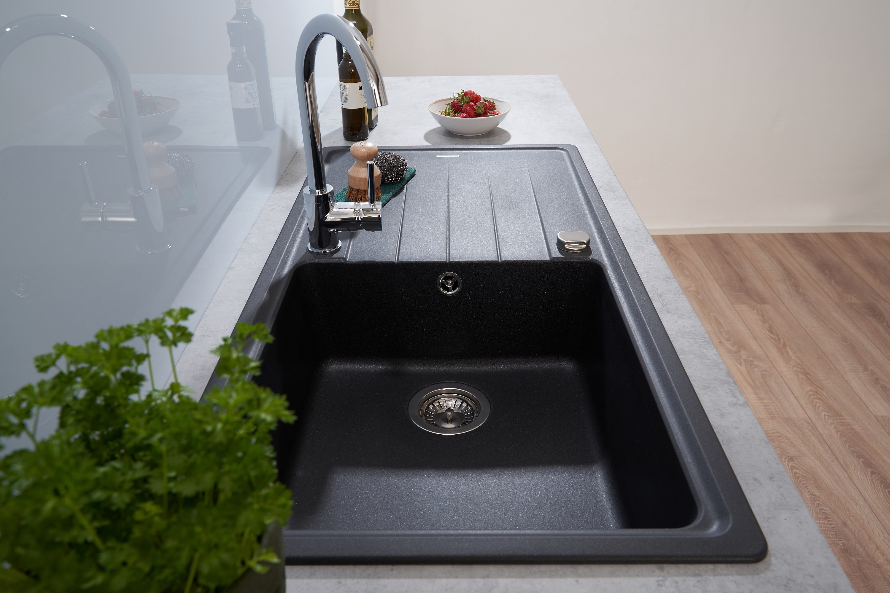 Schwarze Küchenspüle mit Wasserhahn und Geschirr. Weiße Arbeitsplatte, grüne Pflanze.