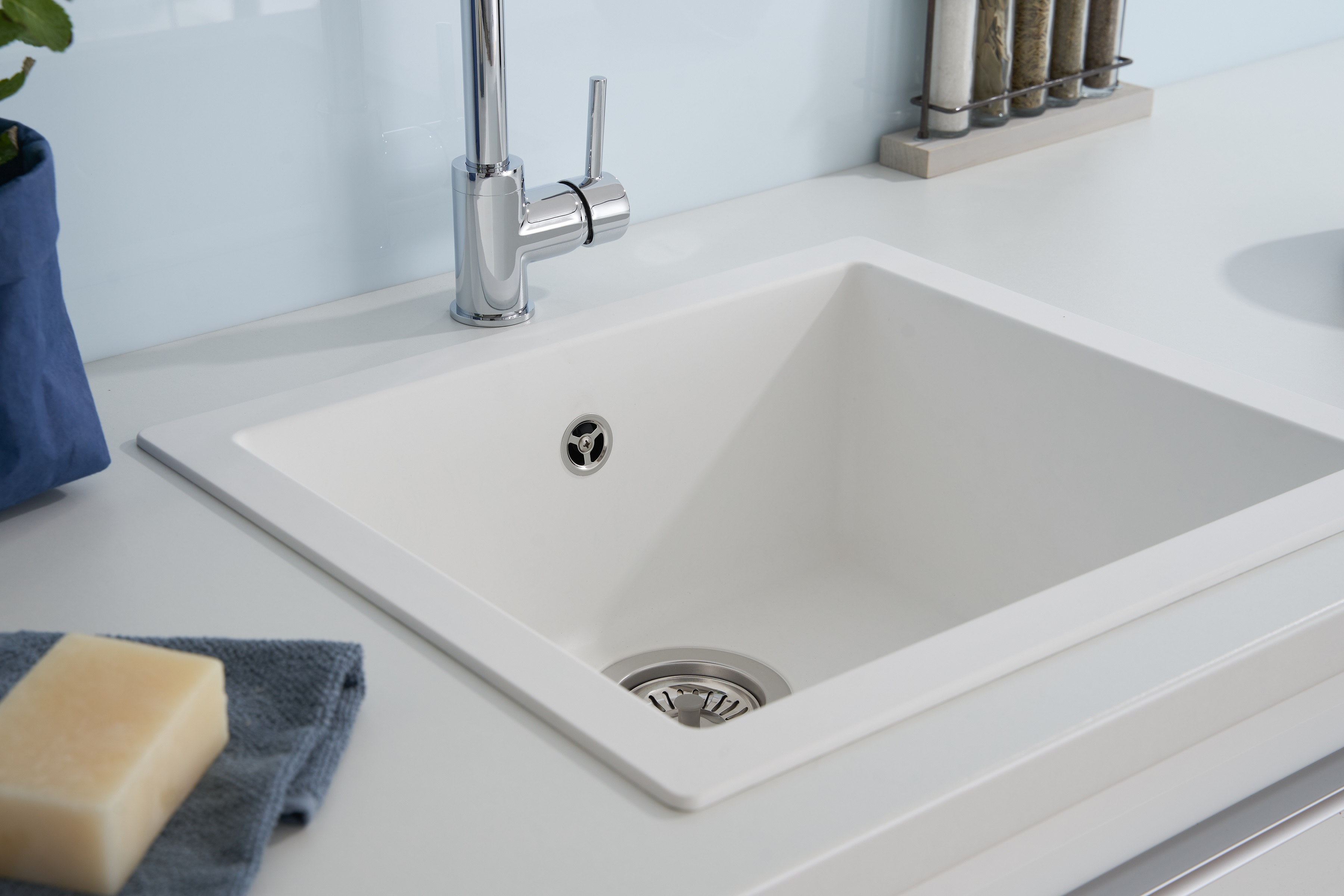 Ein weißes Küchenbecken mit Chromarmatur, Seife und ein blaues Tuch liegen auf der Theke.