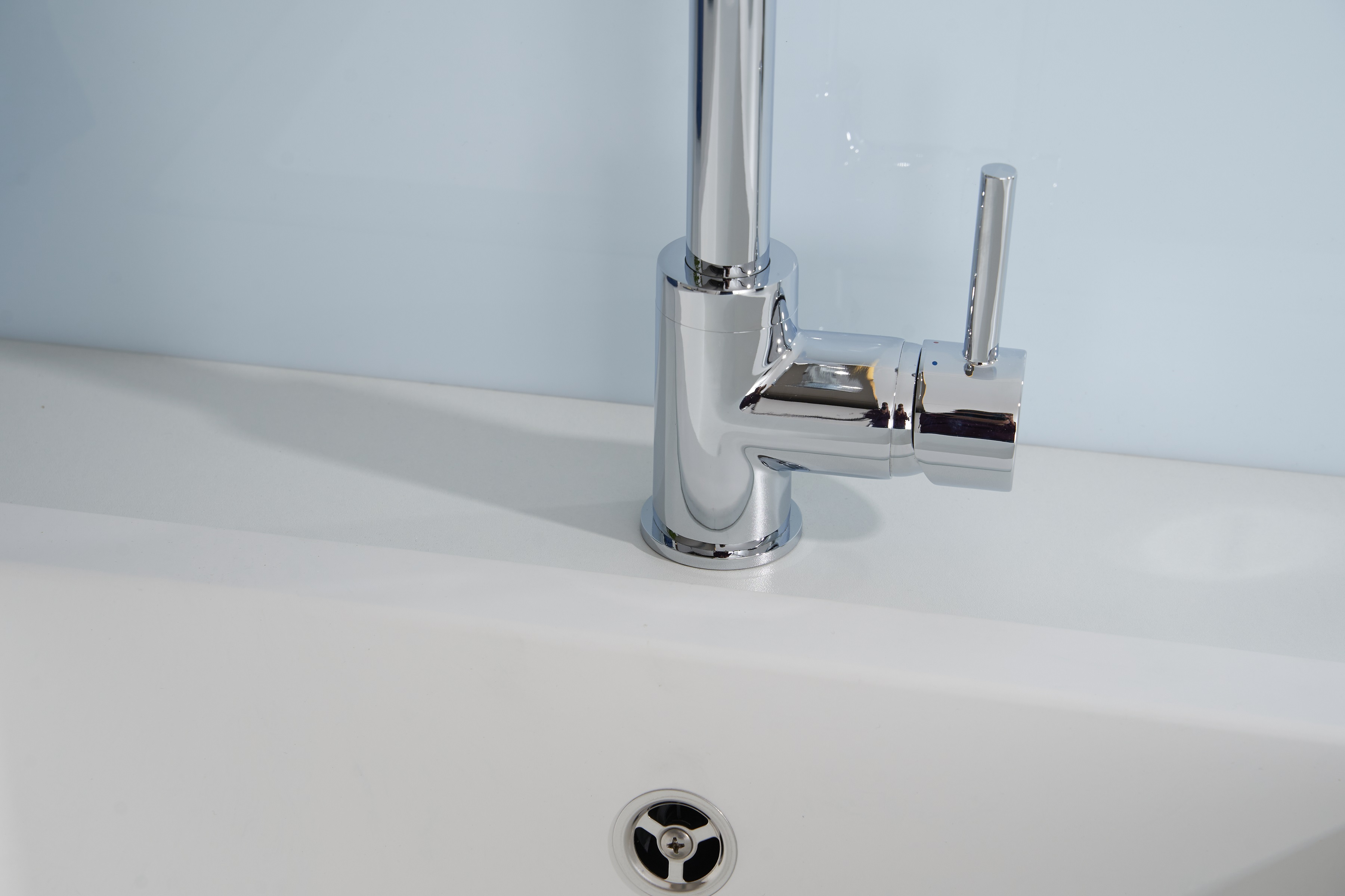Chrom-Wasserhahn auf einem weißen Waschbecken mit hellblauer Wand im Hintergrund.