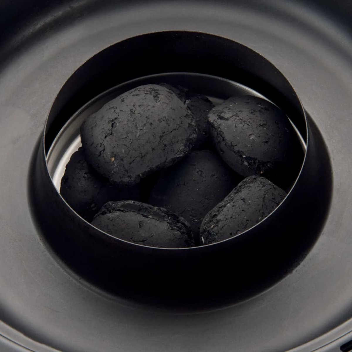 Schwarze Holzkohlebriketts in einer schwarzen Schüssel, bereit zum Grillen.
