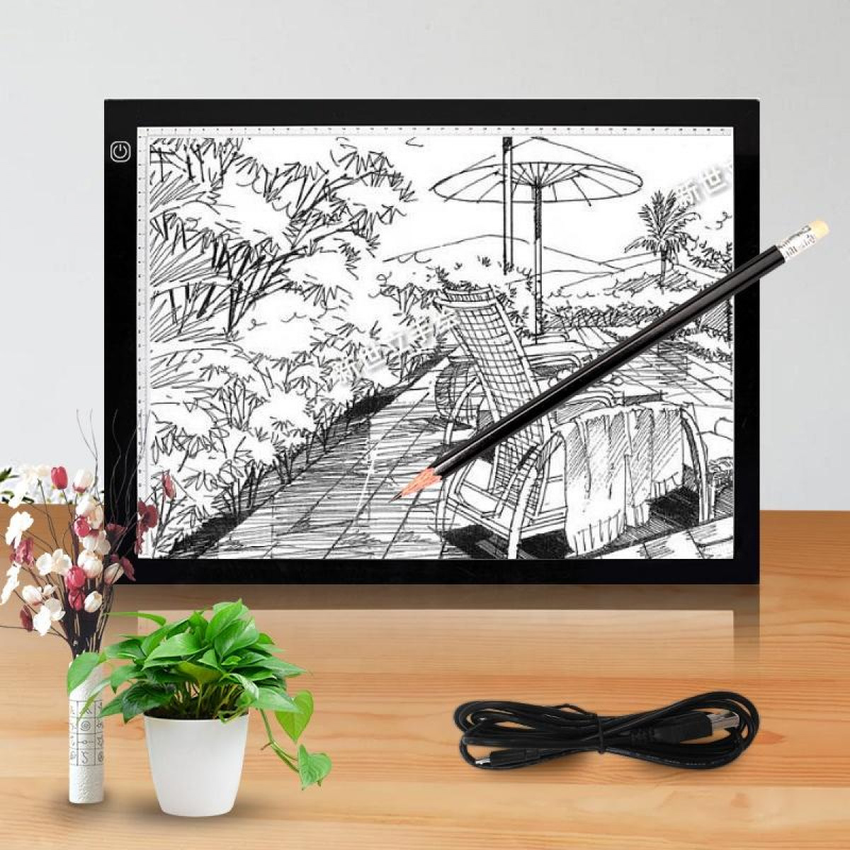 Stół świetlny z rysunkiem. Ołówek nad rysunkiem, rośliną i czarnym kablem.