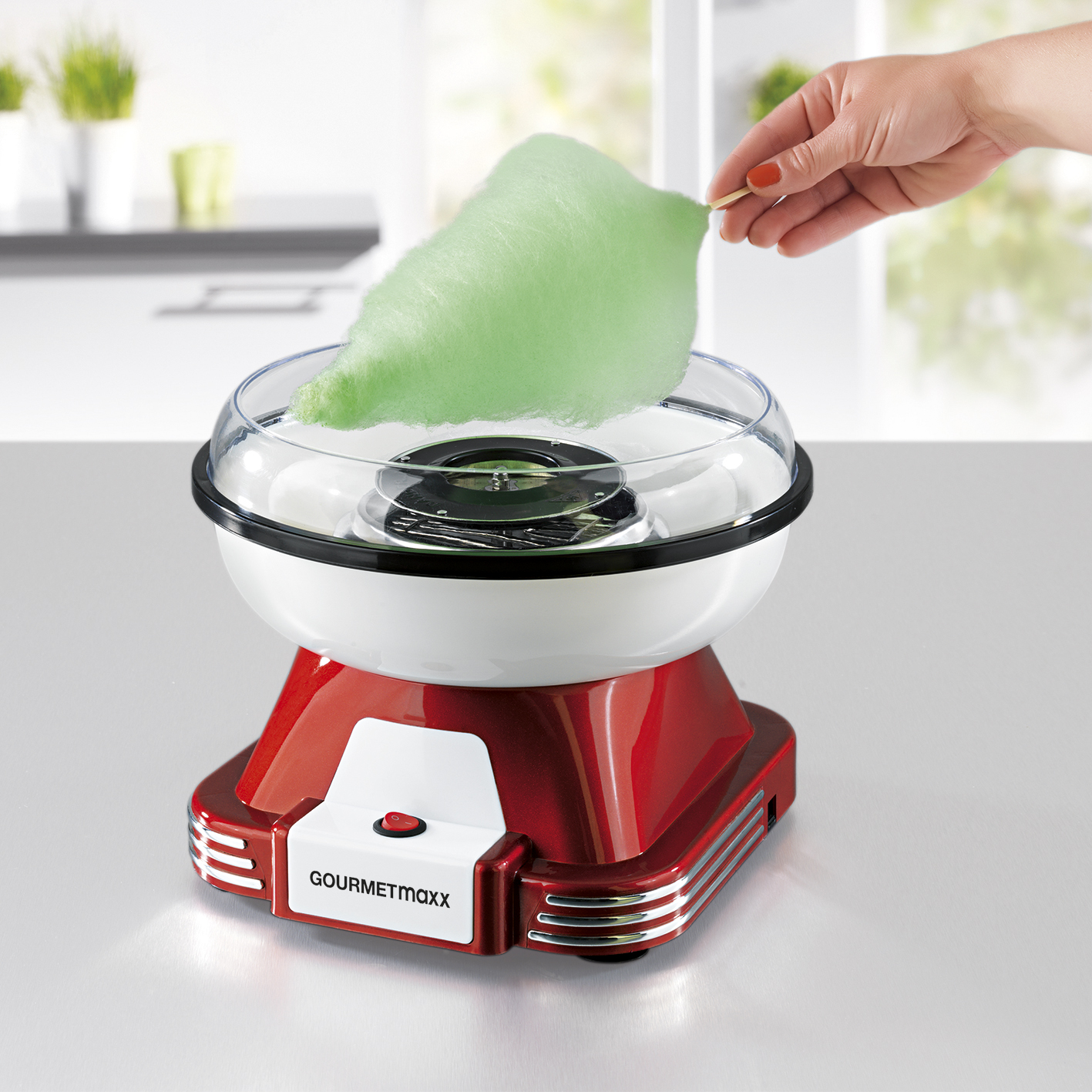 Eine rote Zuckerwattemaschine, aus der eine Person grüne Zuckerwatte zieht.