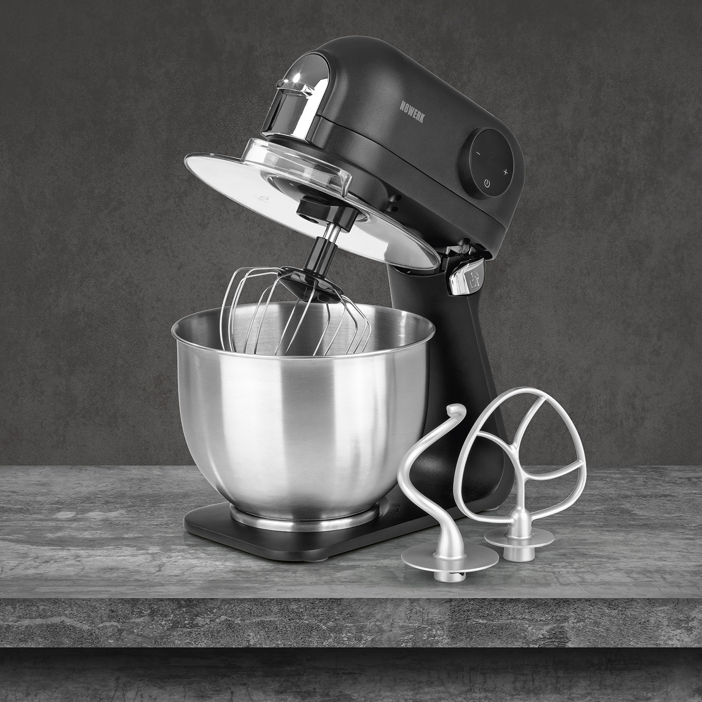 Schwarzer Küchenmixer mit Schüssel, Schneebesen und Knethaken. Dunkelgrauer Hintergrund.